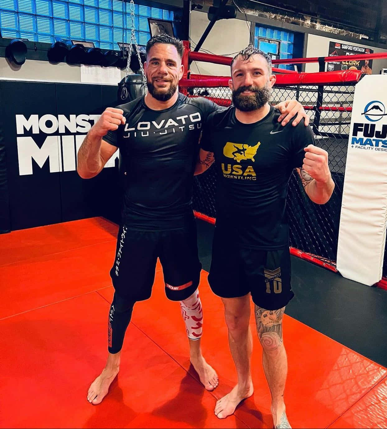 兩名男性MMA拳手在鋪有紅色軟墊及品牌牆壁的健身室內擺姿勢。