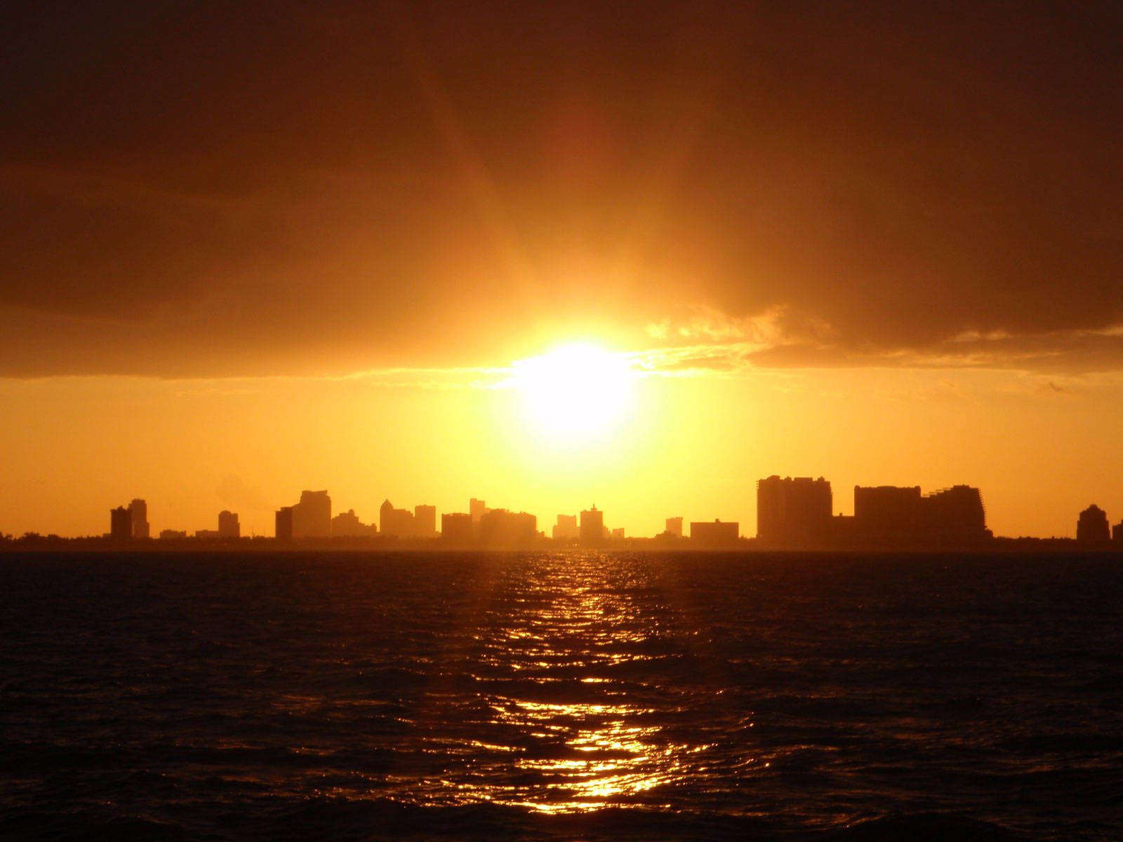 邁阿密壯麗的黃色天空 壁紙 — 金色夕陽將耀眼的光芒投射在漣漪水面上倒映的城市天際線。