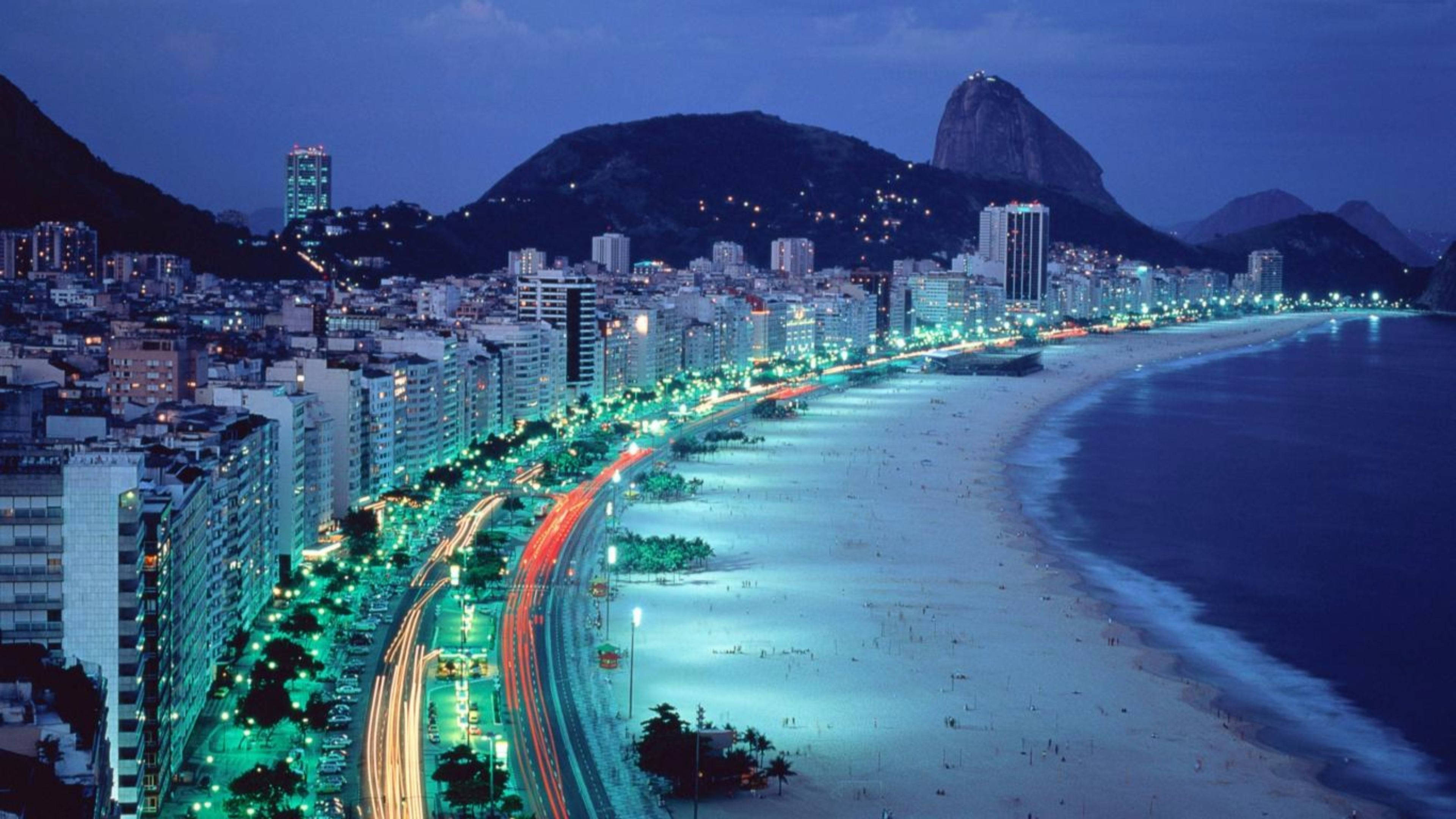 邁阿密海濱夜景 壁紙 — 里約熱內盧科帕卡巴納海灘的航拍圖，黃昏時分，城市燈光閃爍，標誌性的糖麵包山在背景中。
