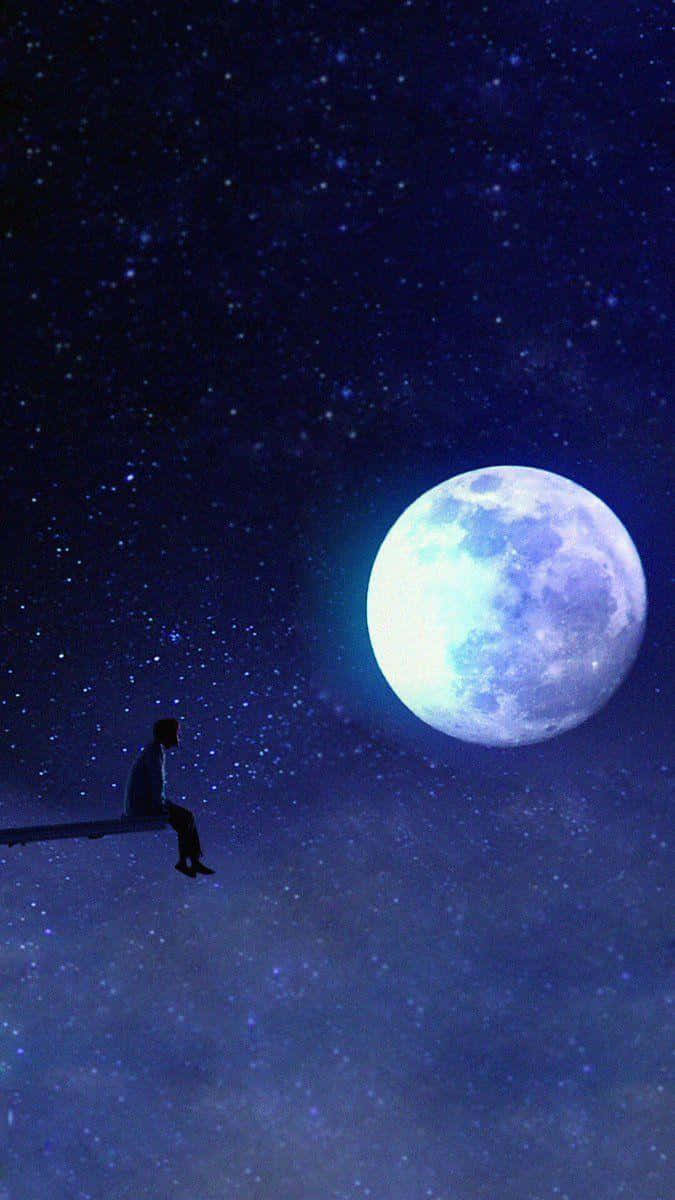 一個人在星空夜空中巨大的發光月亮下坐在長椅上的剪影。