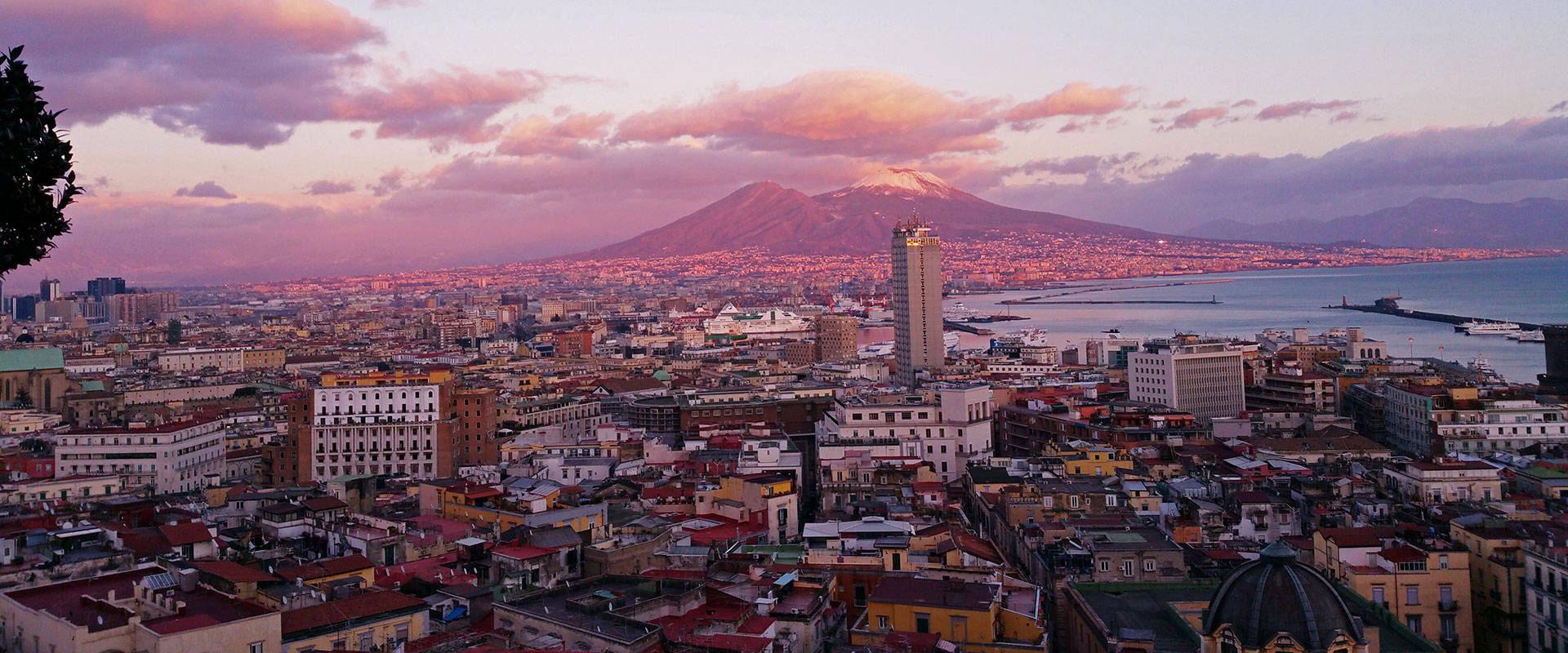 那不勒斯城市全景 壁紙 — 那不勒斯的全景日落景觀，維蘇威火山聳立於城市和海洋之上。