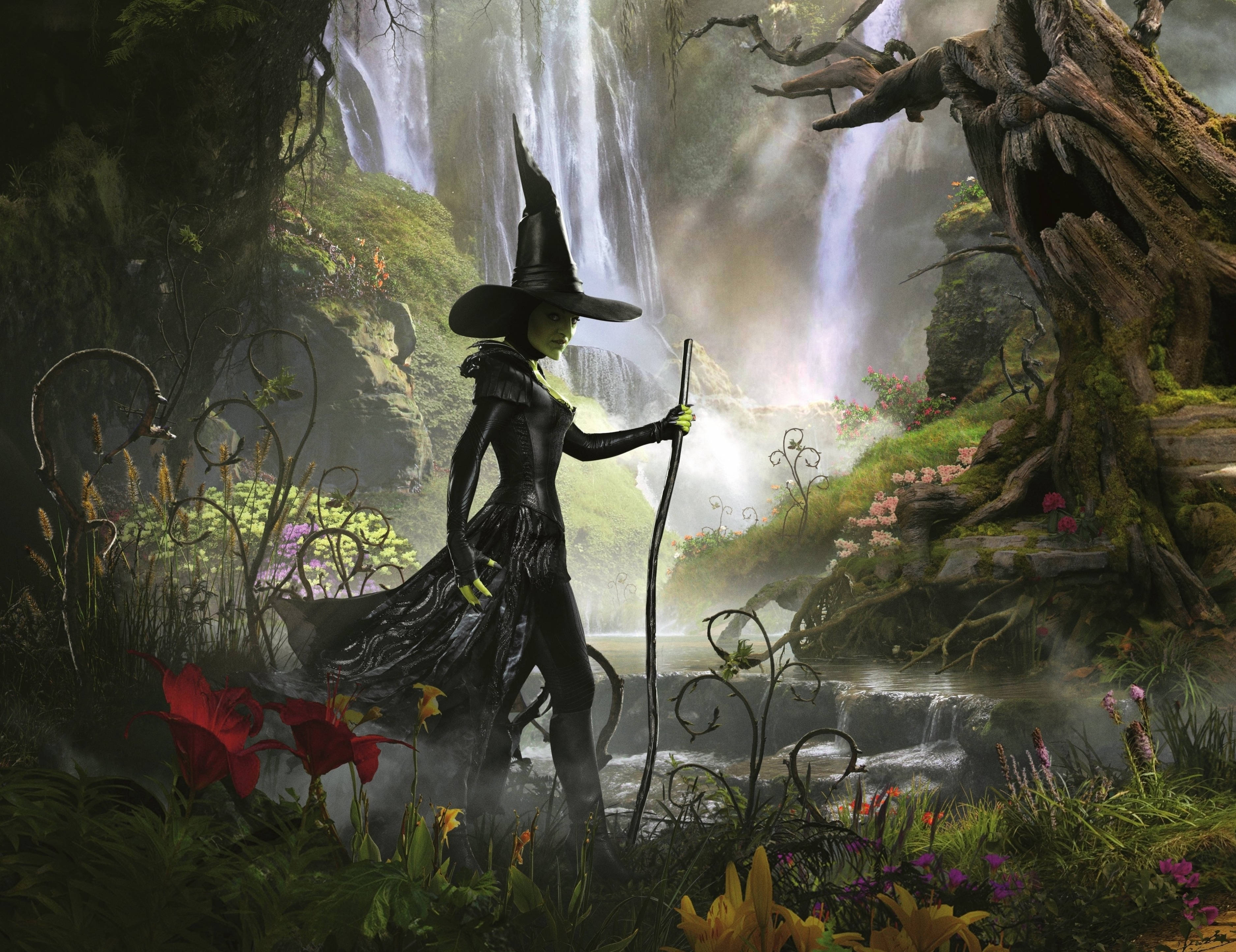 邪惡魔法城堡的魔幻之夜 壁紙 — 一位身穿深色長袍、戴著高帽的女巫，站在迷霧森林中，旁邊有瀑布和鮮豔的花朵。
