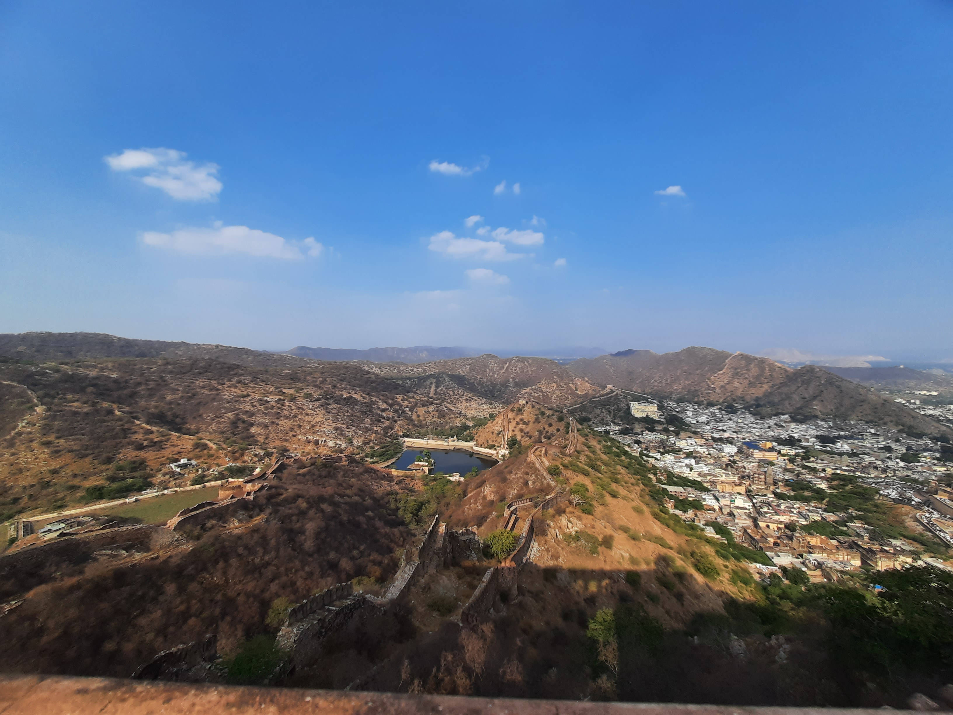 郊區與丘陵地貌 壁紙 — 一個歷史堡壘的 panoramatic 景觀，坐落在乾燥的山丘上，俯瞰著在清澈藍天下延伸的城鎮。
