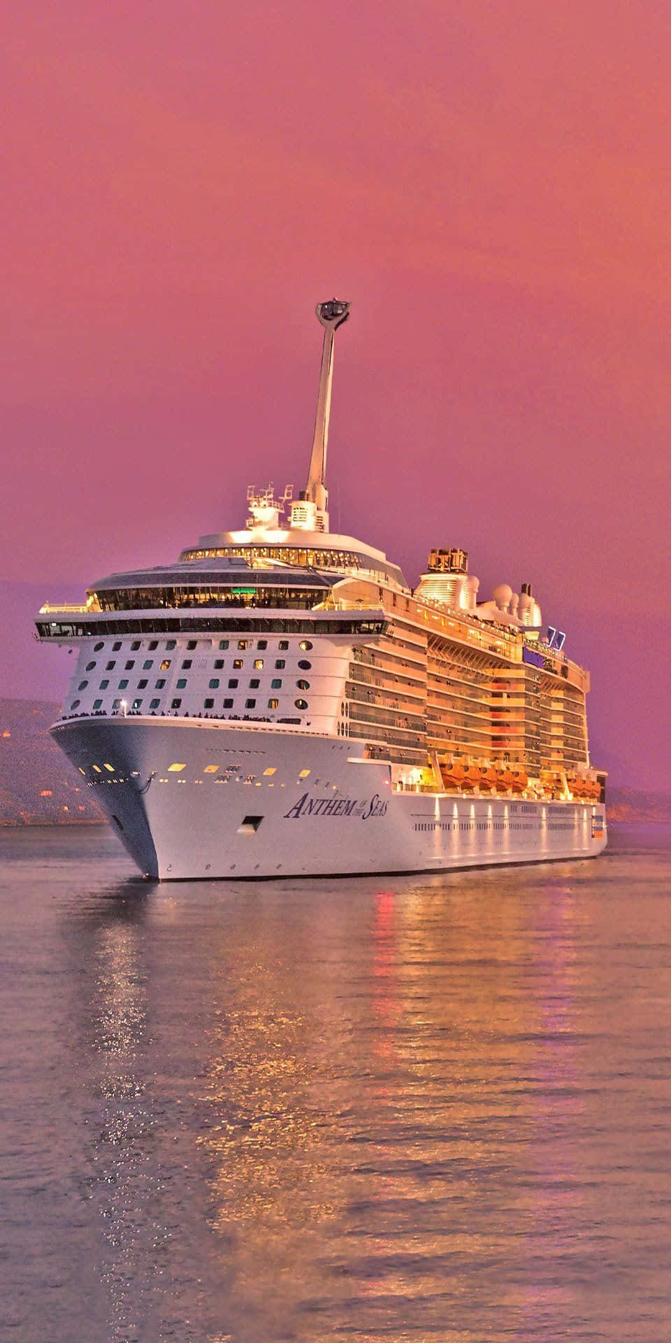 郵輪對著粉紅天空航行 壁紙 — 郵輪 Anthem of the Seas 在充滿活力的粉紅色暮色天空中溫暖地發光，其燈光在平靜的水面上反射。
