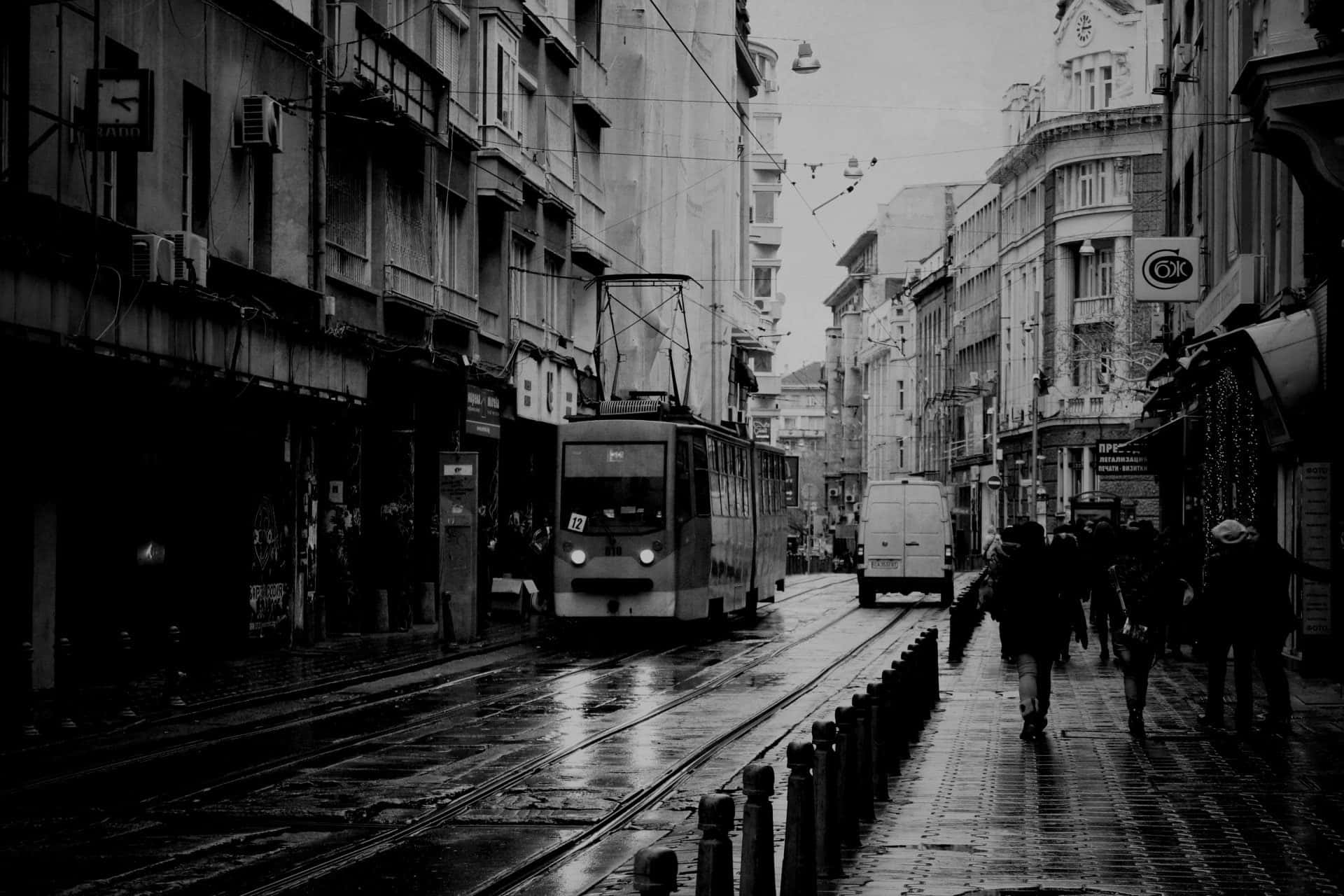 雨中的城市街道，有電車和人們在濕漉漉的鵝卵石上行走。