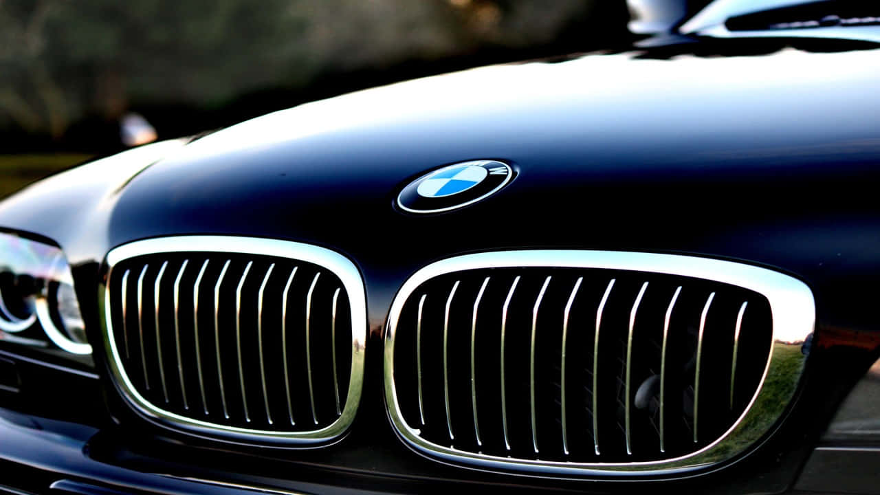 都市環境中的 BMW 車款 壁紙 — 近距離拍攝亮黑色寶馬引擎蓋，在柔和燈光下展示標誌性鍍鉻腎形格柵和圓形標誌。