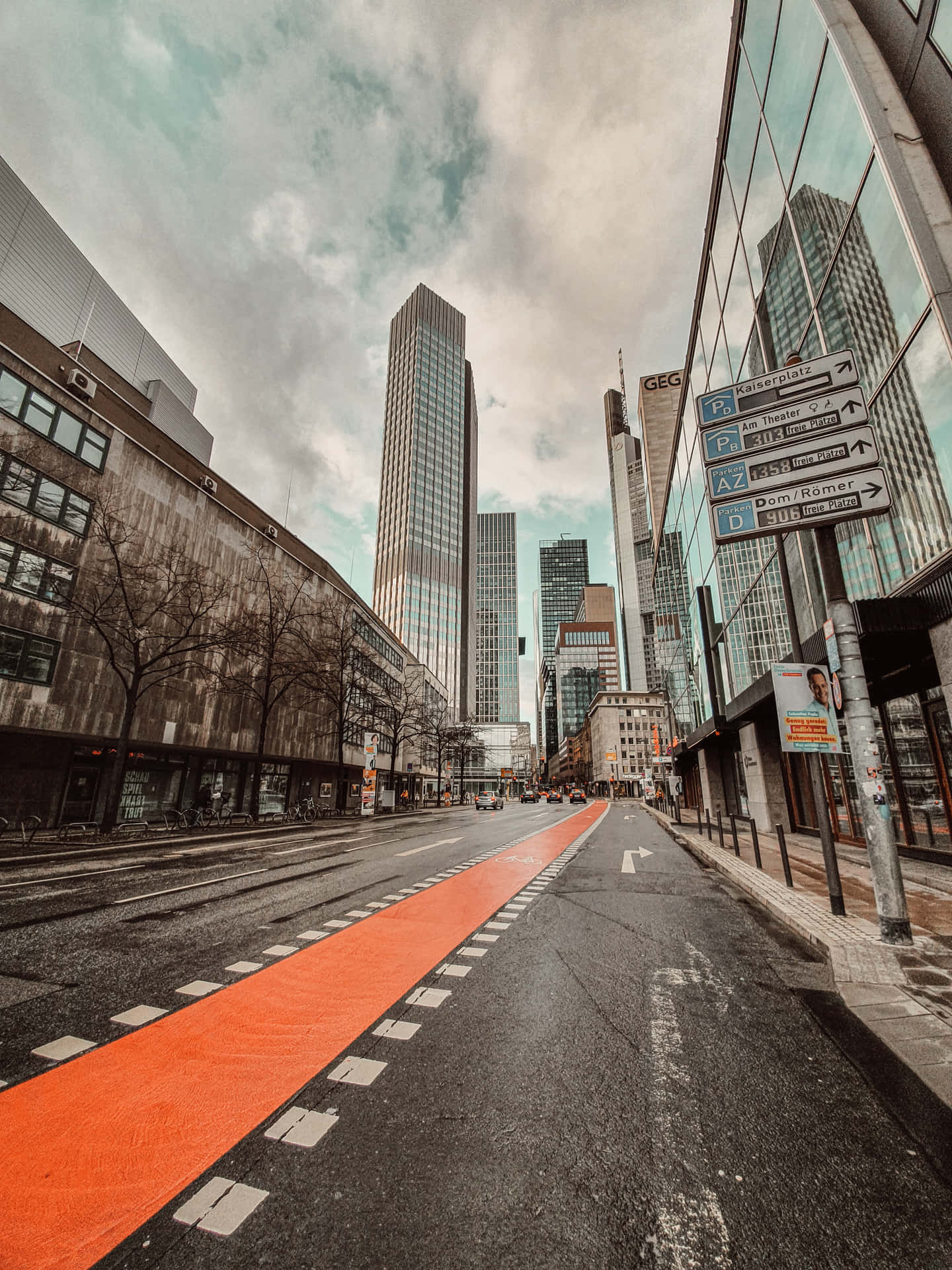 城市街道，有橙色單車徑和高大的玻璃建築，天空多雲。