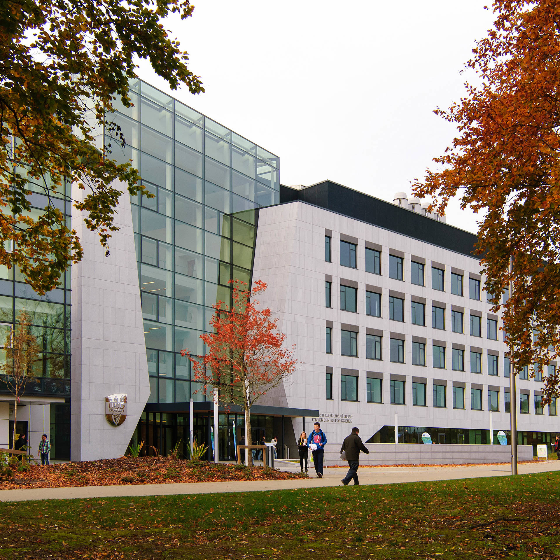 現代大學建築，玻璃和石材外牆，周圍有秋樹和走路的學生。