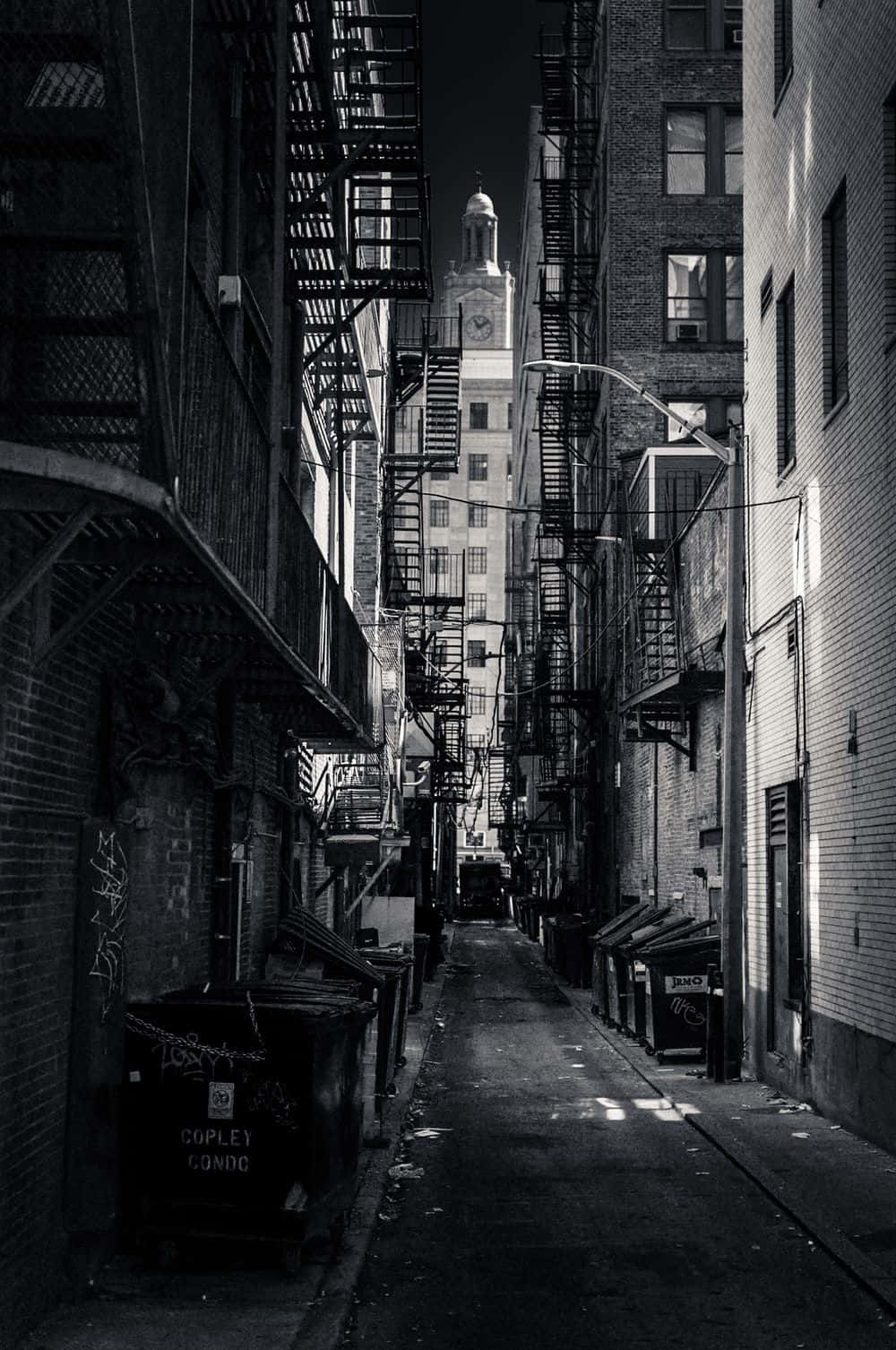 磚砌建築之間的黑白小巷，帶有防火梯和遠處的鐘樓。