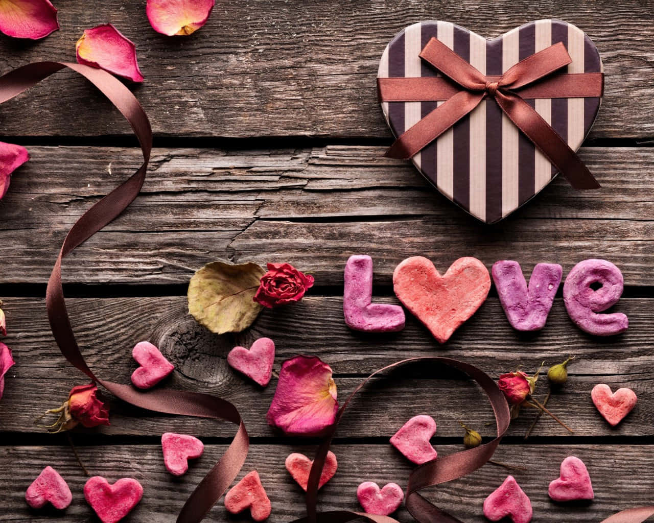 心形禮物盒和粉紅色黏土心形在木桌上拼出 love，並有玫瑰花瓣。