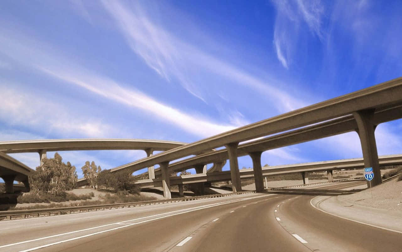 鄉村田野中蜿蜒公路的空中視角 壁紙 — 一覽無遺的景觀，展現分層混凝土高速公路高架橋，上方是充滿活力的藍天和縷縷白雲。