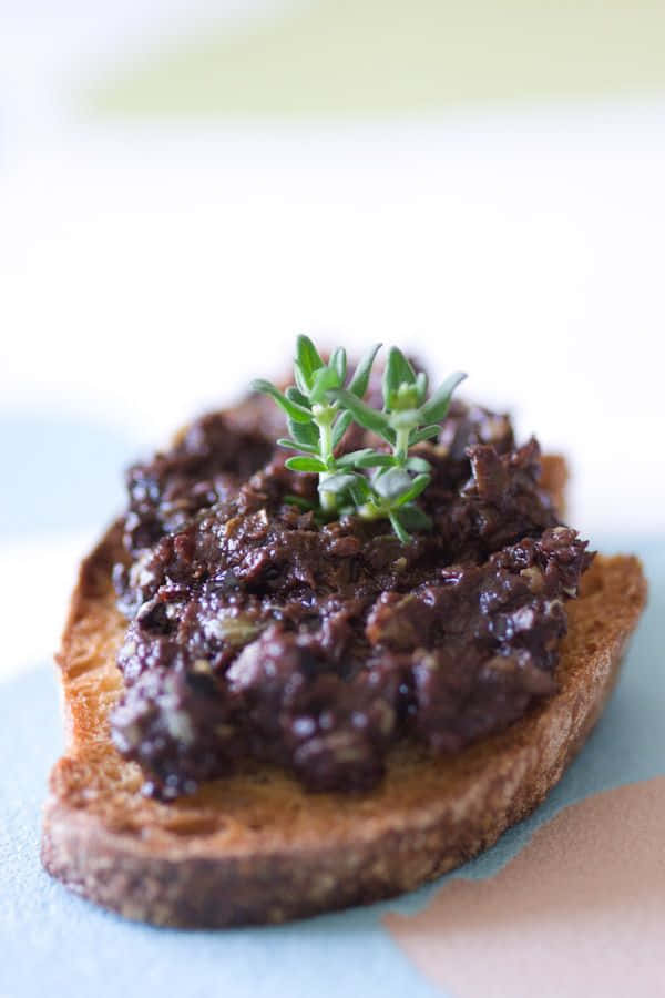 Black Olives 桌布 壁紙 — 鄉村風吐司切片特寫，上面鋪有深色橄欖醬和新鮮百里香枝。