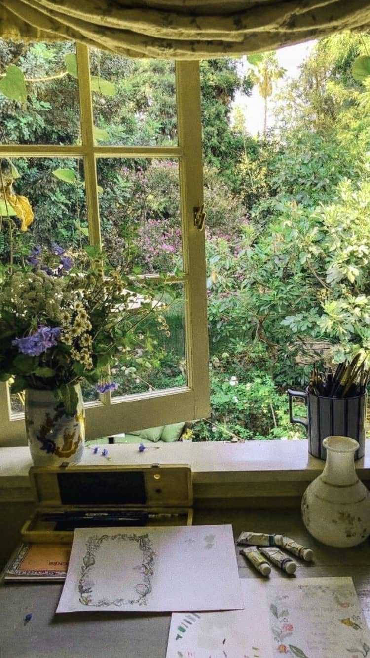 花園窗邊的藝術家書桌，上面有顏料和鮮花