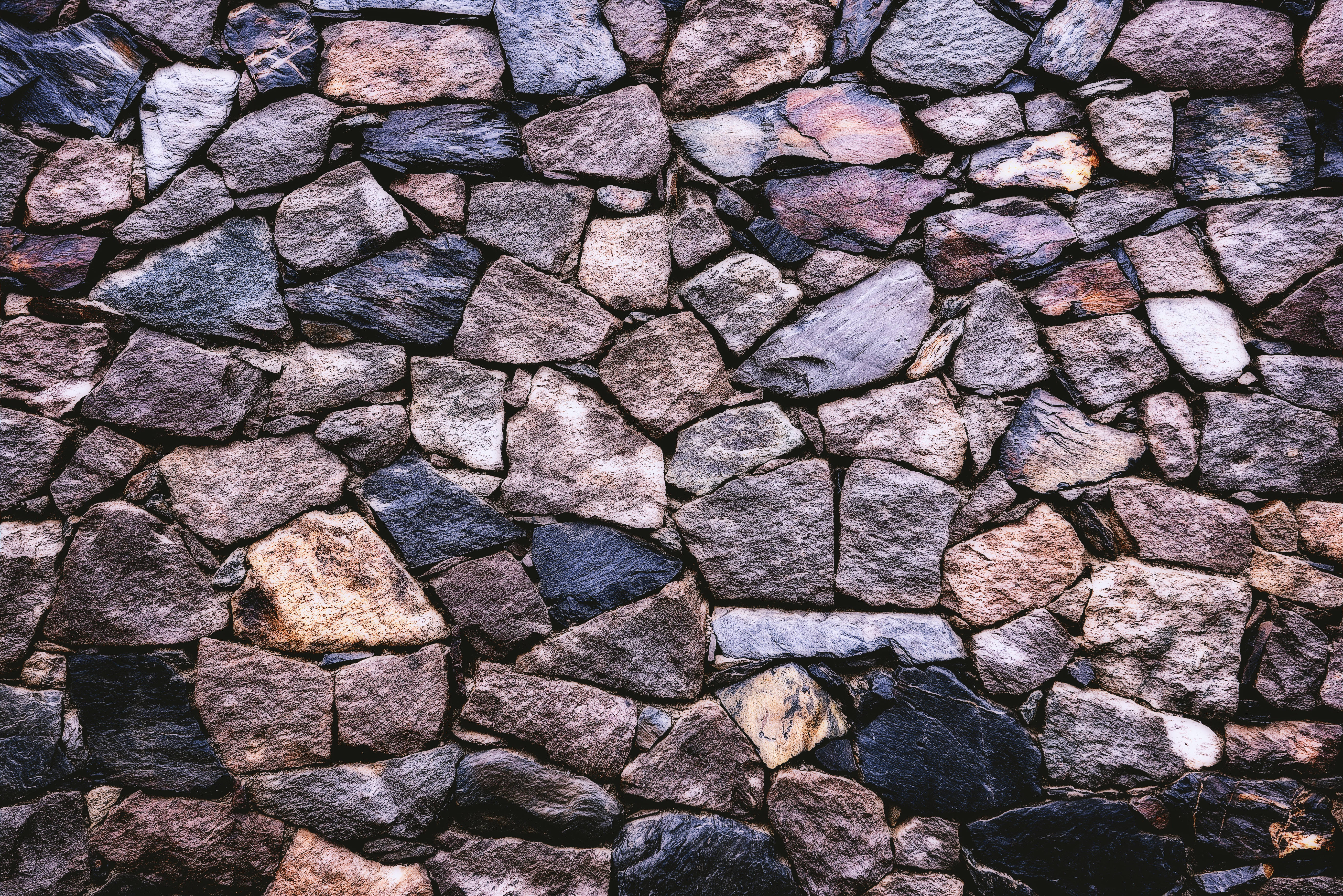 石頭 桌布 壁紙 — 鄉村風格石牆的近距離特寫，呈現多種大地色調和粗糙質感。