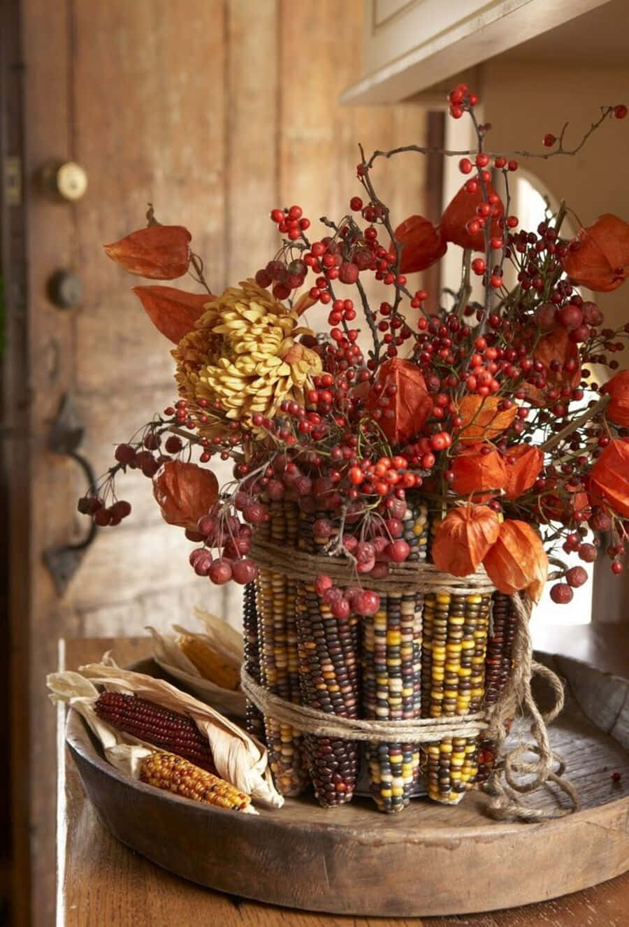 Fall Crafts 桌布 壁紙 — 鄉村風秋季中心裝飾，以玉米皮、紅莓和乾橙燈籠置於編織玉米芯花瓶中。