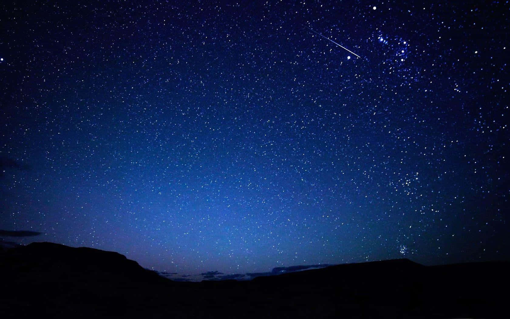 一顆流星劃過繁星點點的夜空，上方是黑暗的山巒剪影。