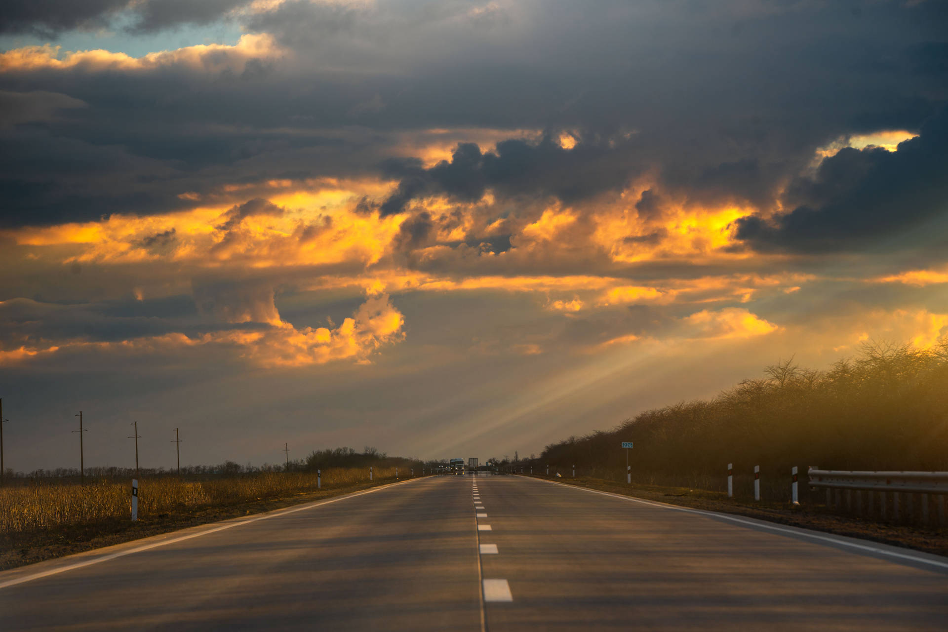 夕陽映照在長長的空曠道路上，伴隨著戲劇性的雲彩和金色光芒。