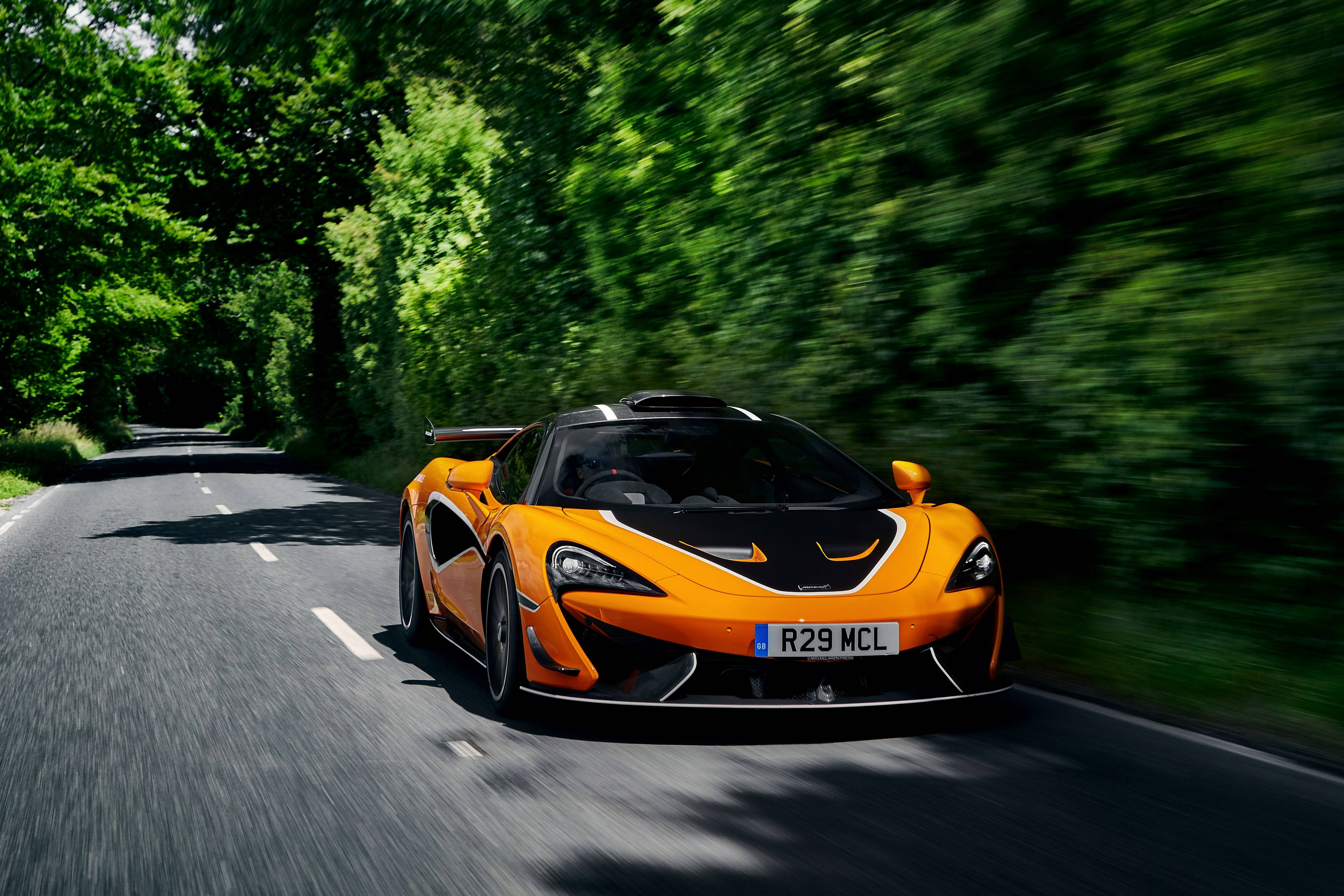 鄉間賽道上的賽車 壁紙 — 一輛充滿活力的橙色McLaren跑車在樹木成蔭的道路上飛馳，動態模糊效果強調了其速度。