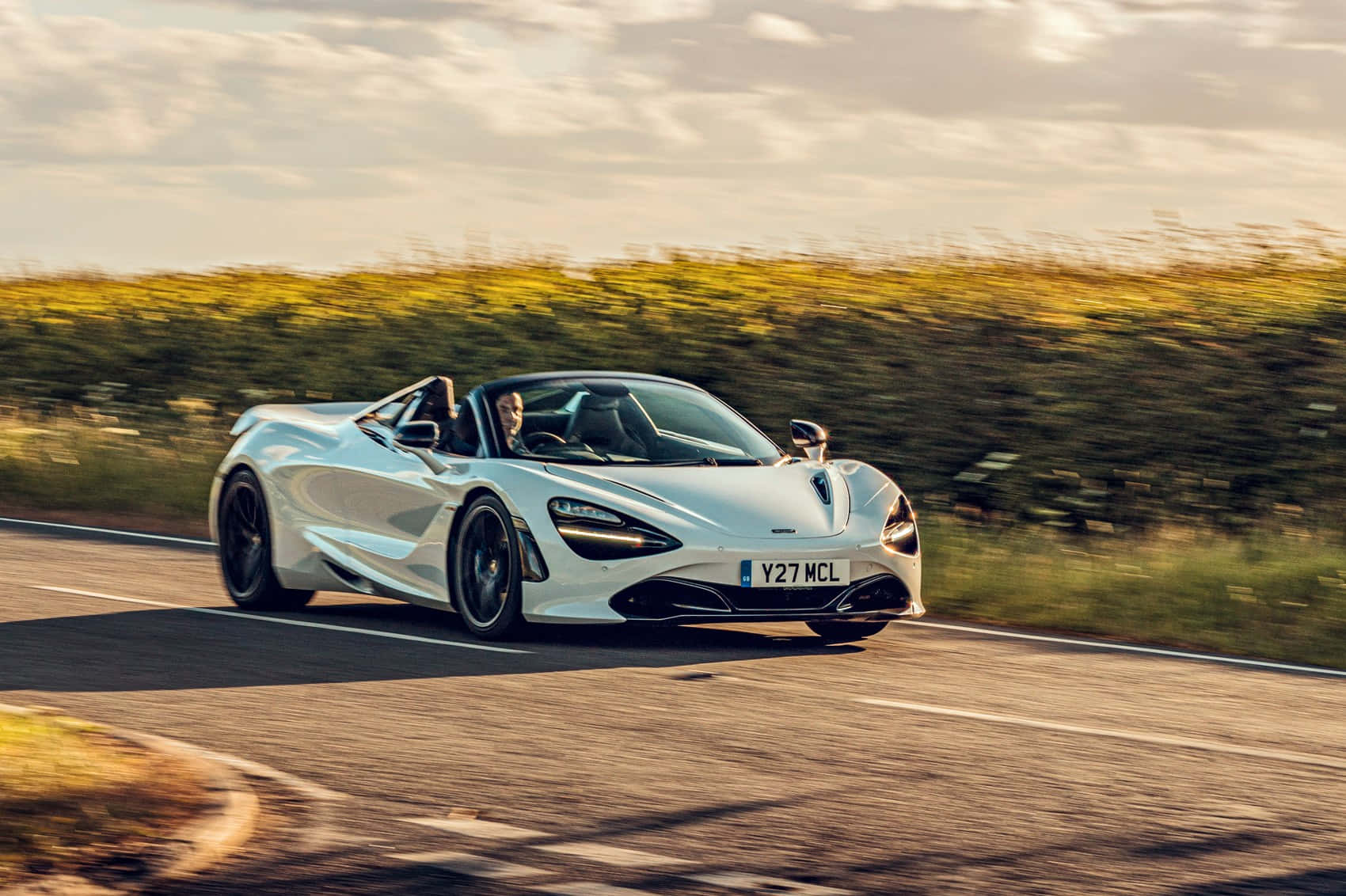 白色McLaren 720S Spider在日落時分行駛在蜿蜒的道路上。
