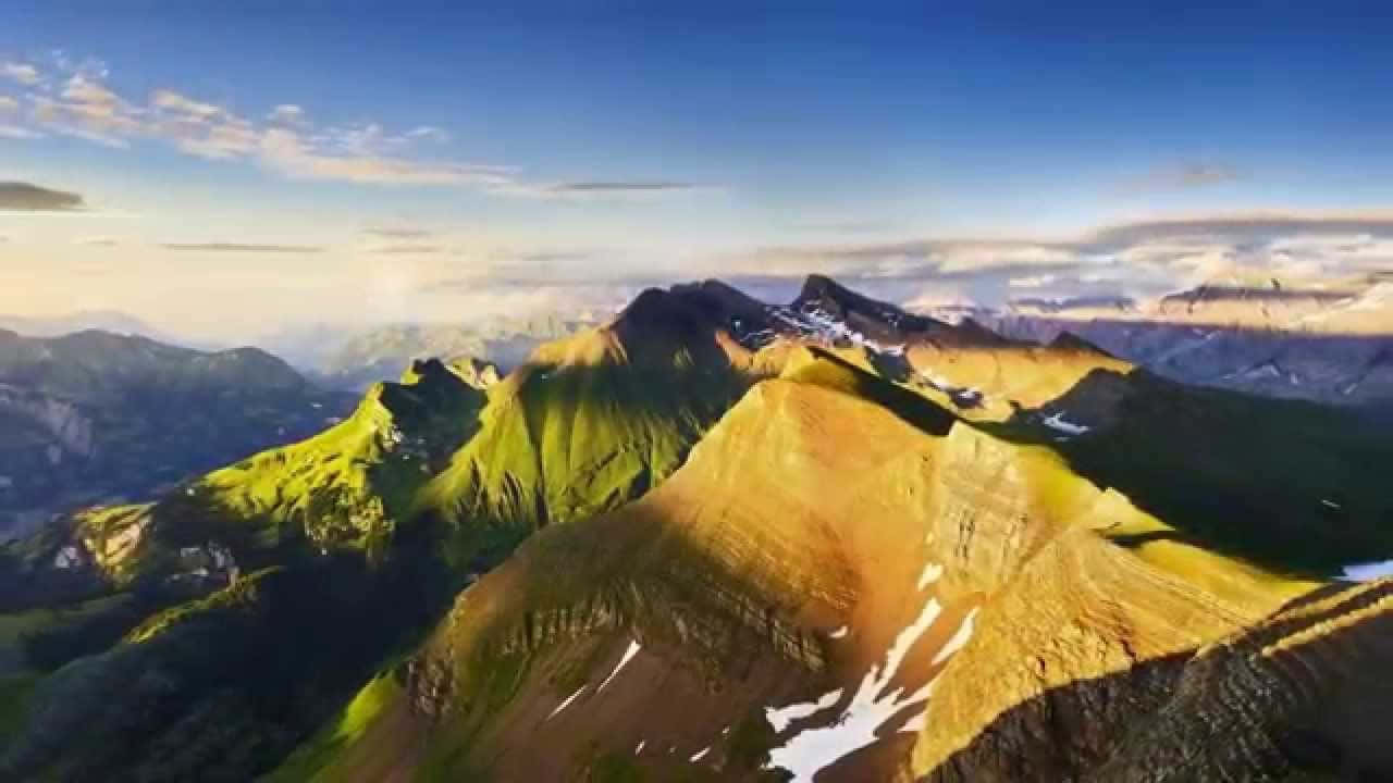 崎嶇的山峰沐浴在金色陽光中，藍天下有雪塊。