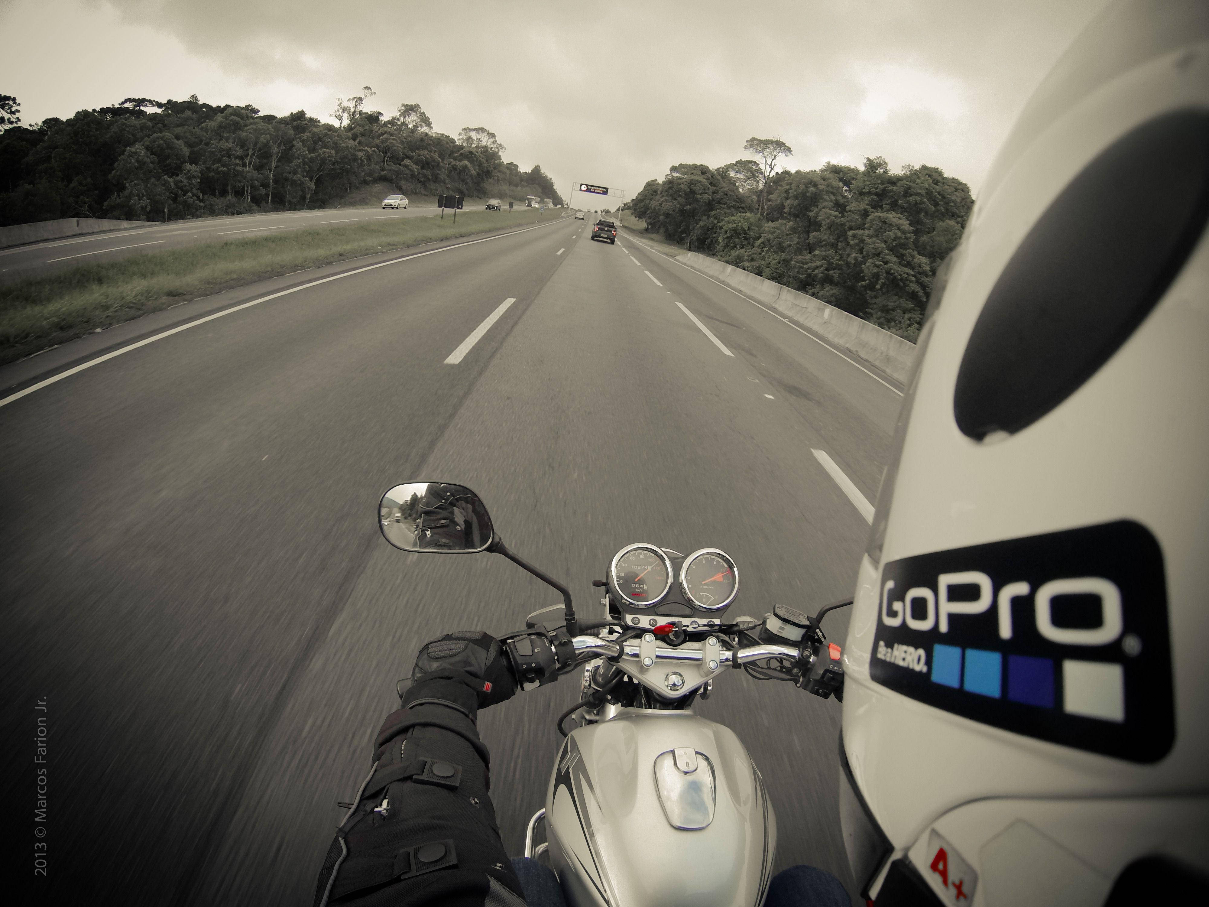 配備 GoPro 的摩托車頭盔 壁紙 — 第一人稱視角，一名電單車手在潮濕的高速公路上飛馳，兩旁是茂密的綠色森林，天空多雲。