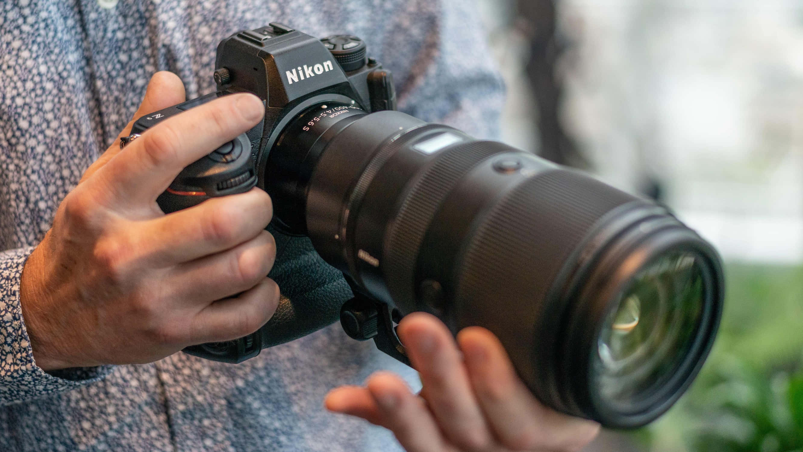 特寫鏡頭，雙手握持帶有遠攝鏡頭的Nikon DSLR相機。