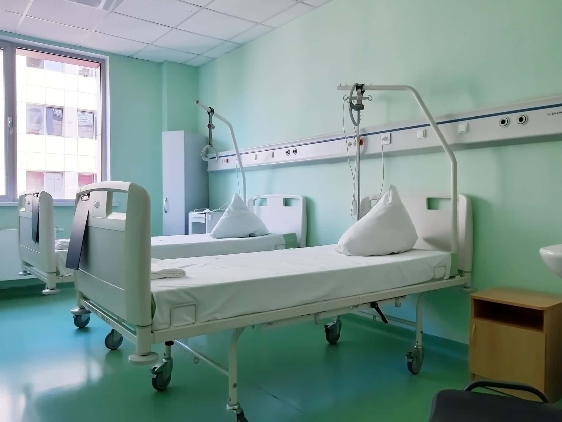 兩張醫院病床在一個有綠色牆壁和窗戶的乾淨醫療室內。