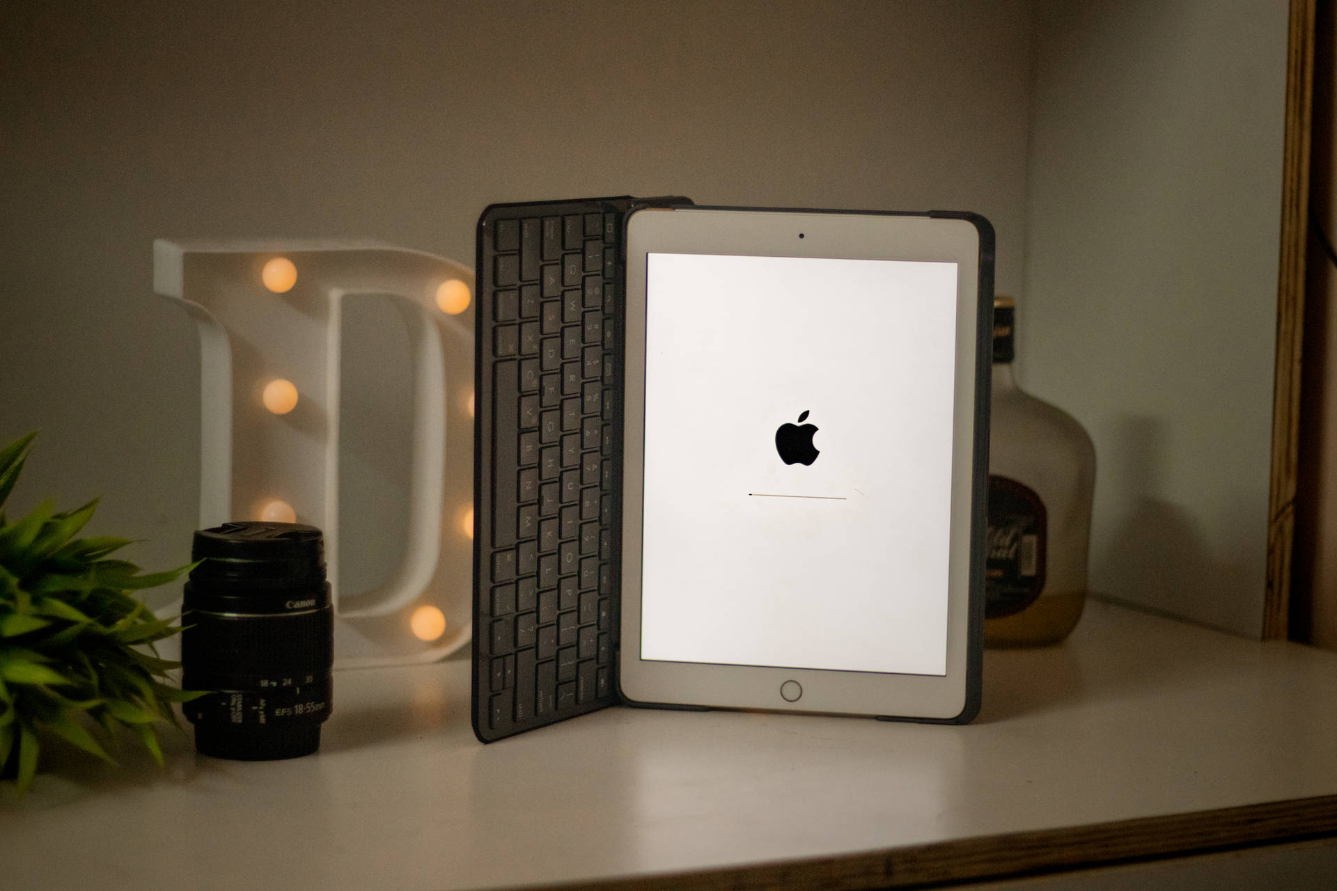 iPad 配備鍵盤保護套，顯示 Apple 標誌，旁邊有發光字母 D 相機鏡頭和植物。