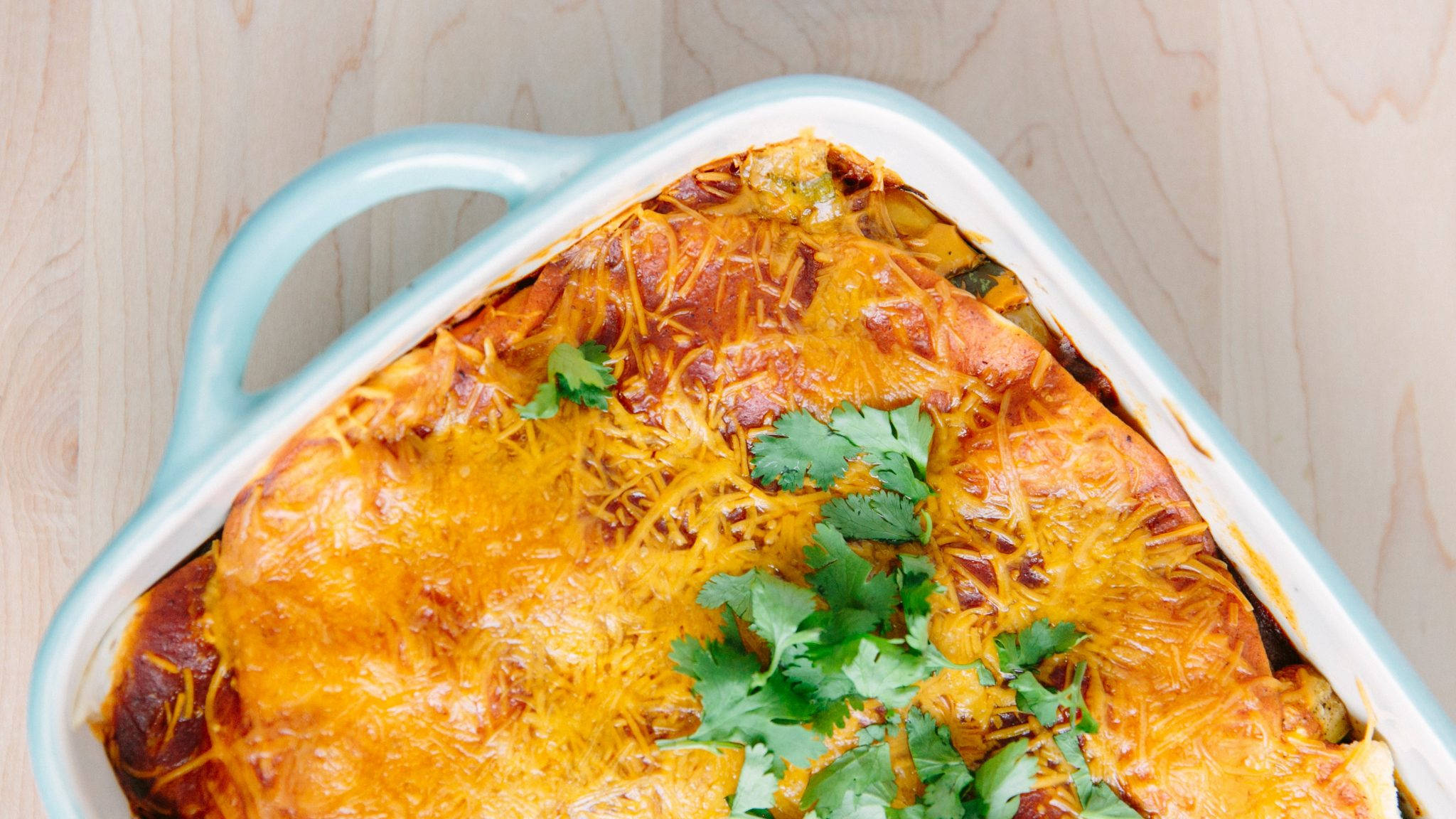 配奶酪莎莎醬的白色盤 enchiladas 壁紙 — 一個金黃色的芝士砂鍋，上面撒上新鮮芫荽，放在淺藍色烤盤中，置於木質表面上。