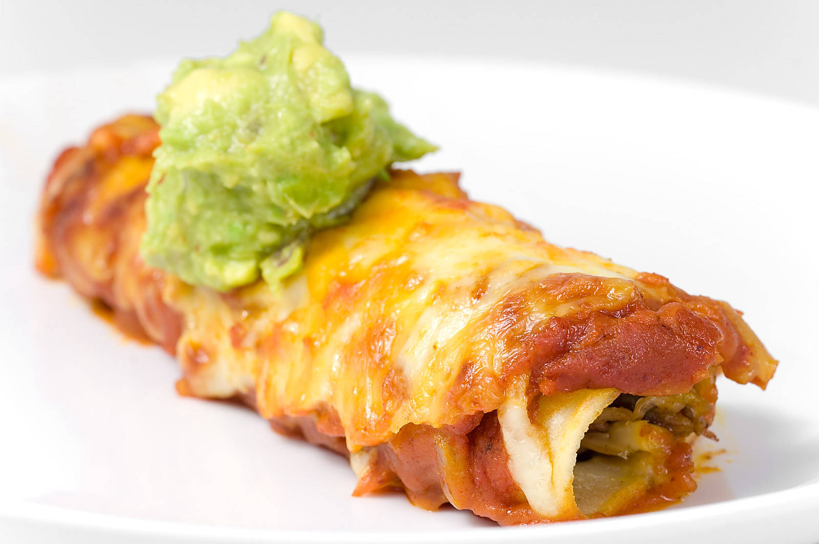 配新鮮牛油果醬的美味 enchiladas 卷 壁紙 — 一個芝士焗玉米餅的特寫，淋上紅醬，上面放上新鮮鱷梨醬，放在白色碟子上。