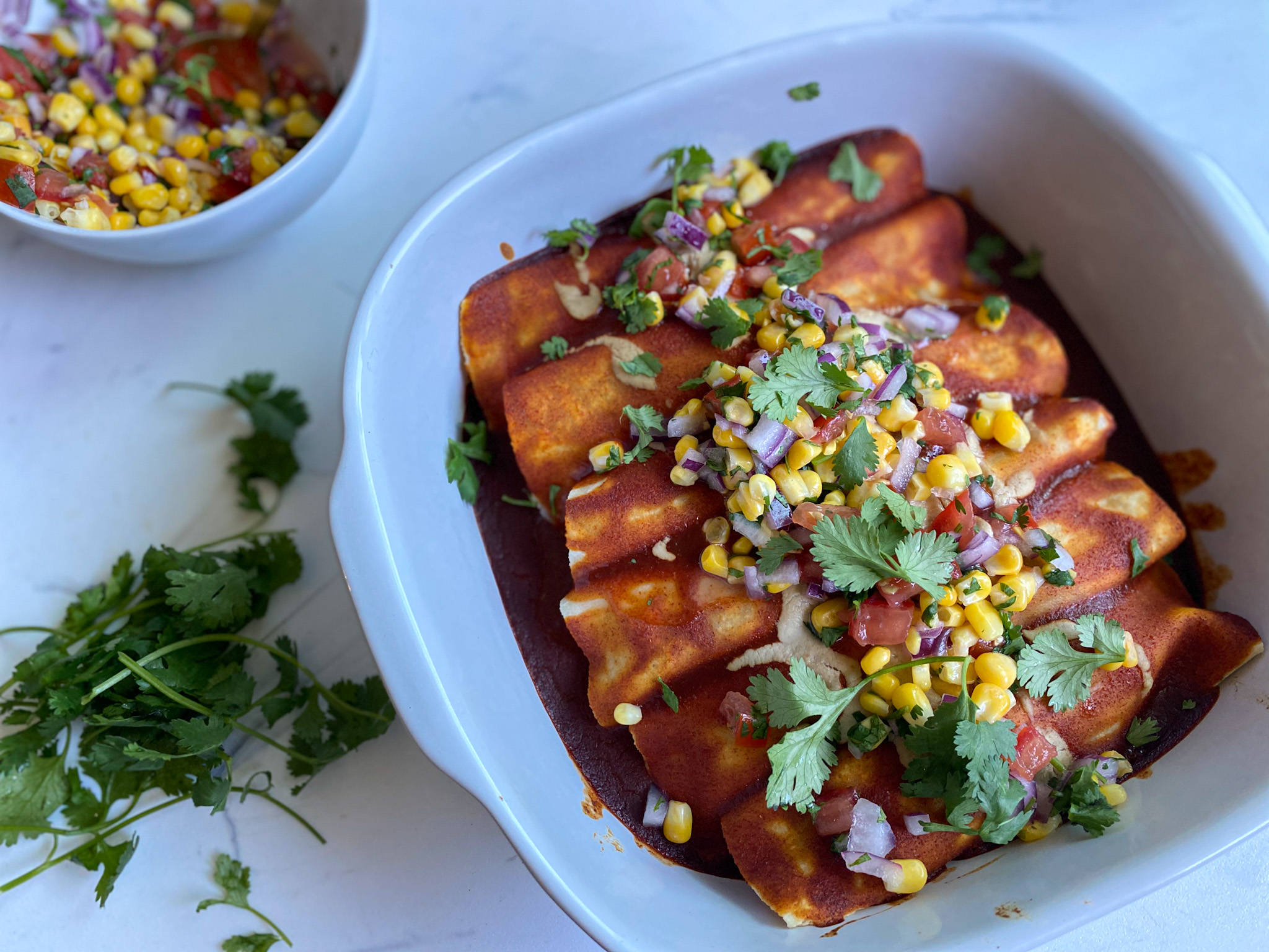 配新鮮蔬菜的誘人 enchiladas 壁紙 — 白色碟子盛載金黃色的墨西哥捲餅，淋上紅醬，並以新鮮粟米、芫荽和洋蔥作點綴。