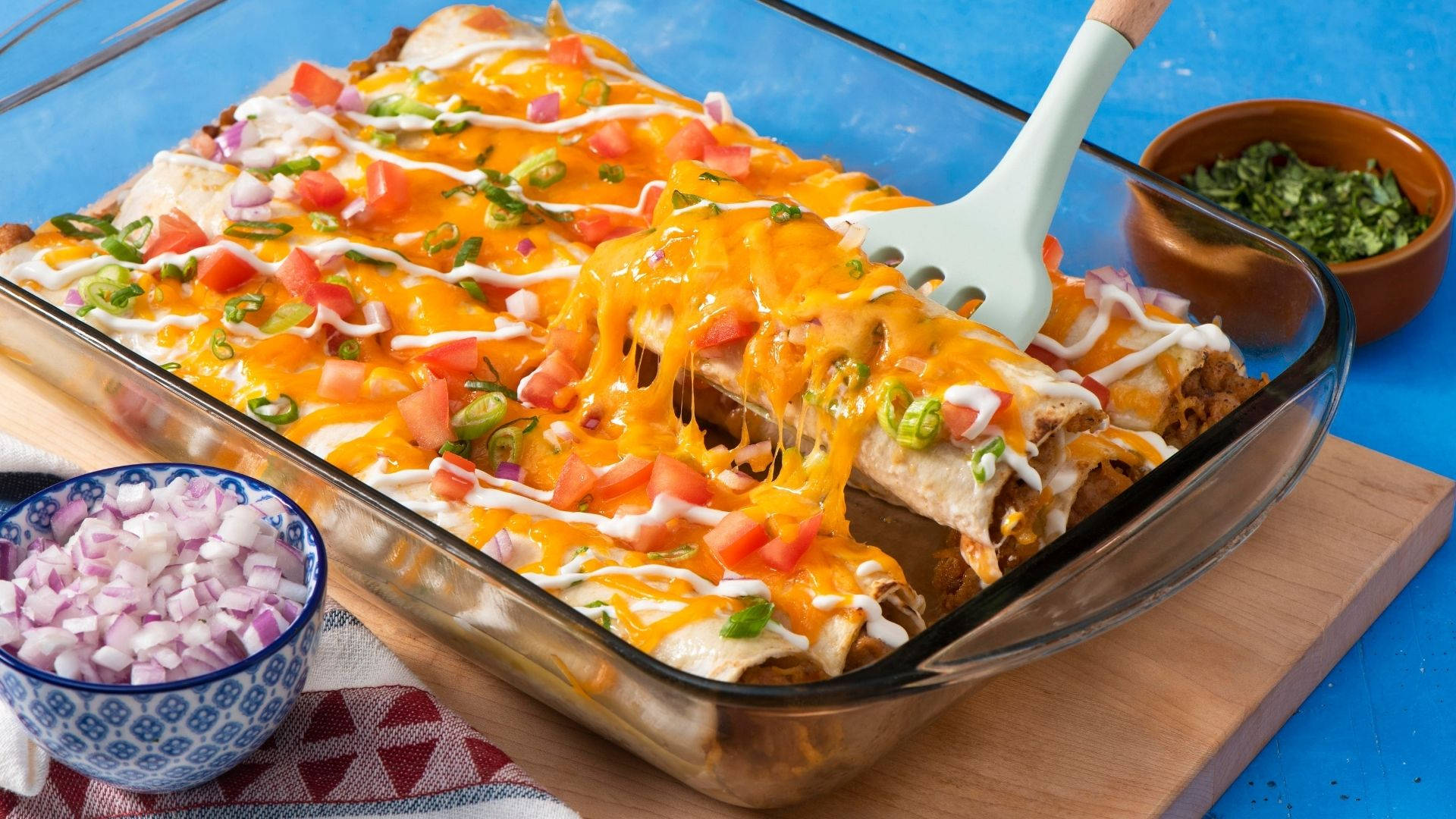配洋蔥的烤奶酪 enchiladas 壁紙 — 金黃芝士玉米卷餅，配上番茄粒和青辣椒，盛載於玻璃烤盤中。