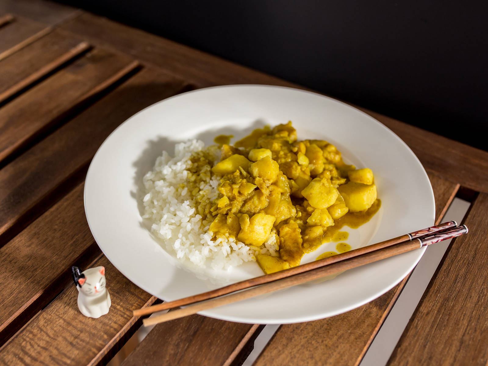 木桌上的一碗咖喱飯、筷子和貓公仔。