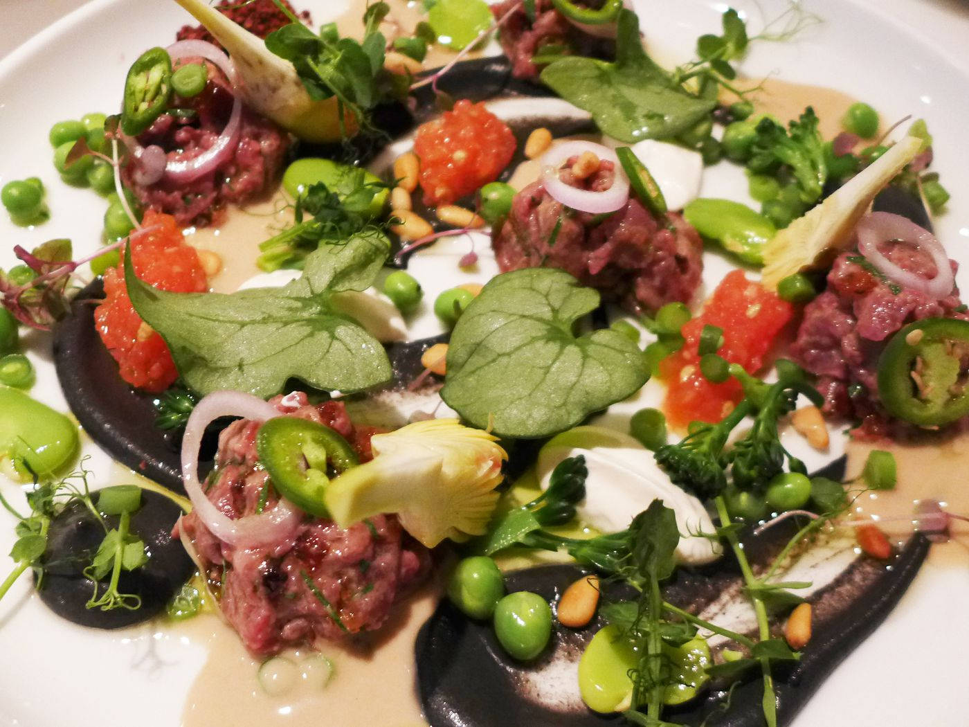 配羅勒沙拉的牛柳塔塔 壁紙 — 一款美食級牛肉他他菜餚，在白碟上以微型蔬菜、豌豆、墨西哥辣椒和奶油醬汁藝術性地擺盤。