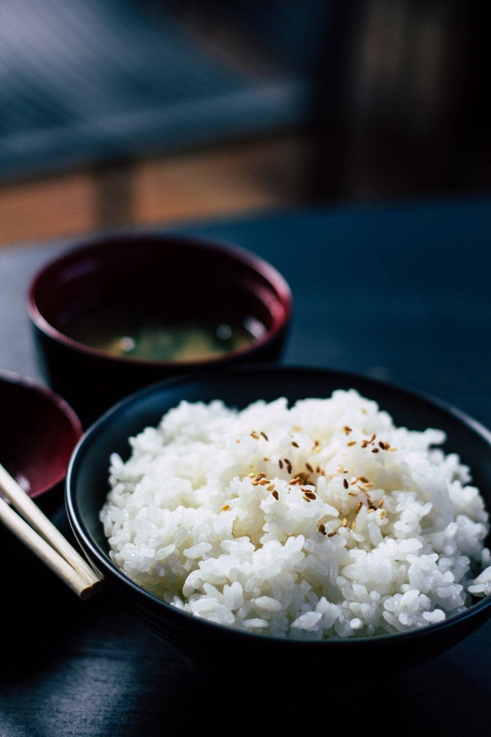 配菜的豐盛飯碗 壁紙 — 一個黑色碗中盛載的蒸白米飯近距離特寫，上面撒有烤芝麻，旁邊放著一個紅色漆器杯的味噌湯。