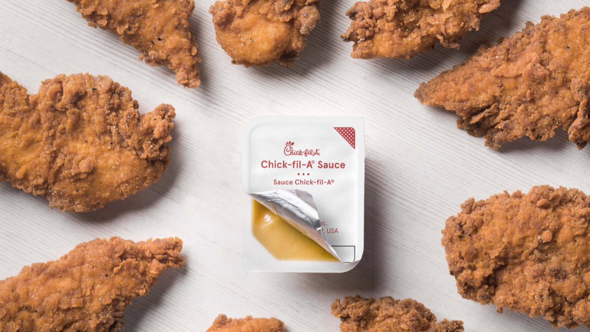 配醬料的雞塊 壁紙 — 金黃色的炸雞塊圍繞著一個Chick-fil-A醬料包在淺色木質表面上。