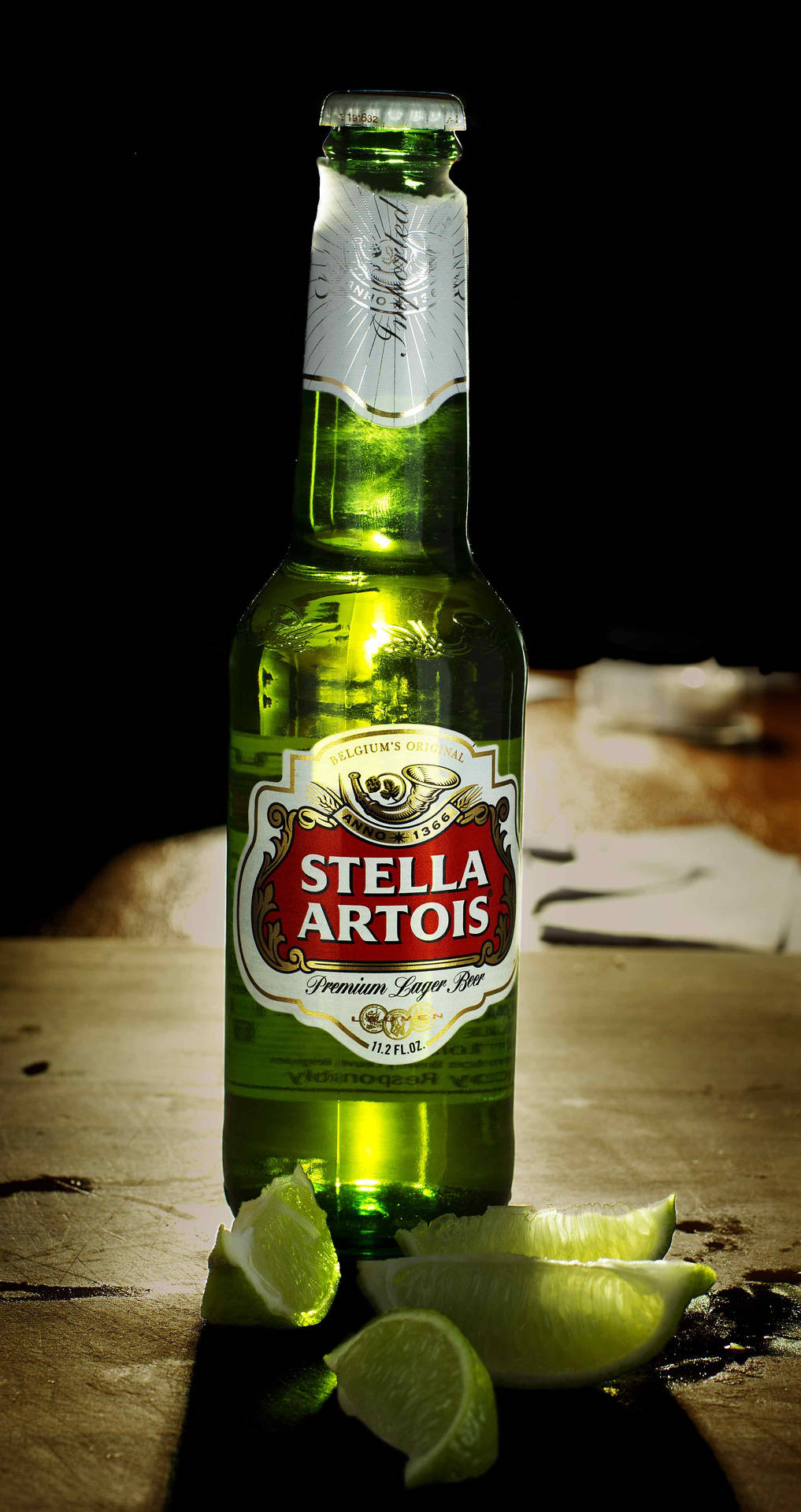 綠色Stella Artois啤酒瓶配以青檸角，放在木桌上，聚光燈下。