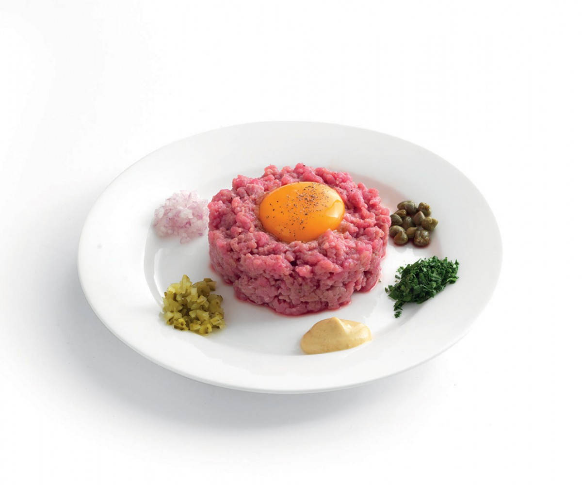 白色碟子上配有生蛋黃和配菜的牛肉他他。