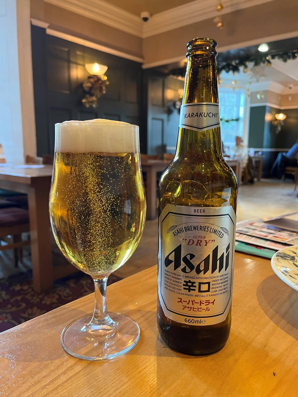 酒吧內朝日超乾啤酒 壁紙 — 一支冰凍的朝日超乾啤酒和一杯金色氣泡啤酒放在舒適酒吧的木桌上。