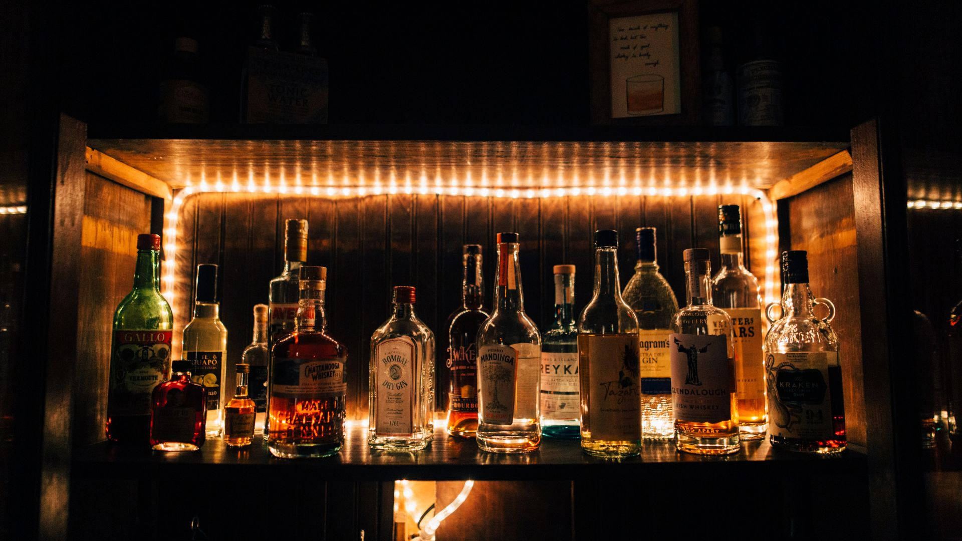 木架上展示各種酒瓶，由溫暖的串燈照亮，位於黑暗的酒吧中。