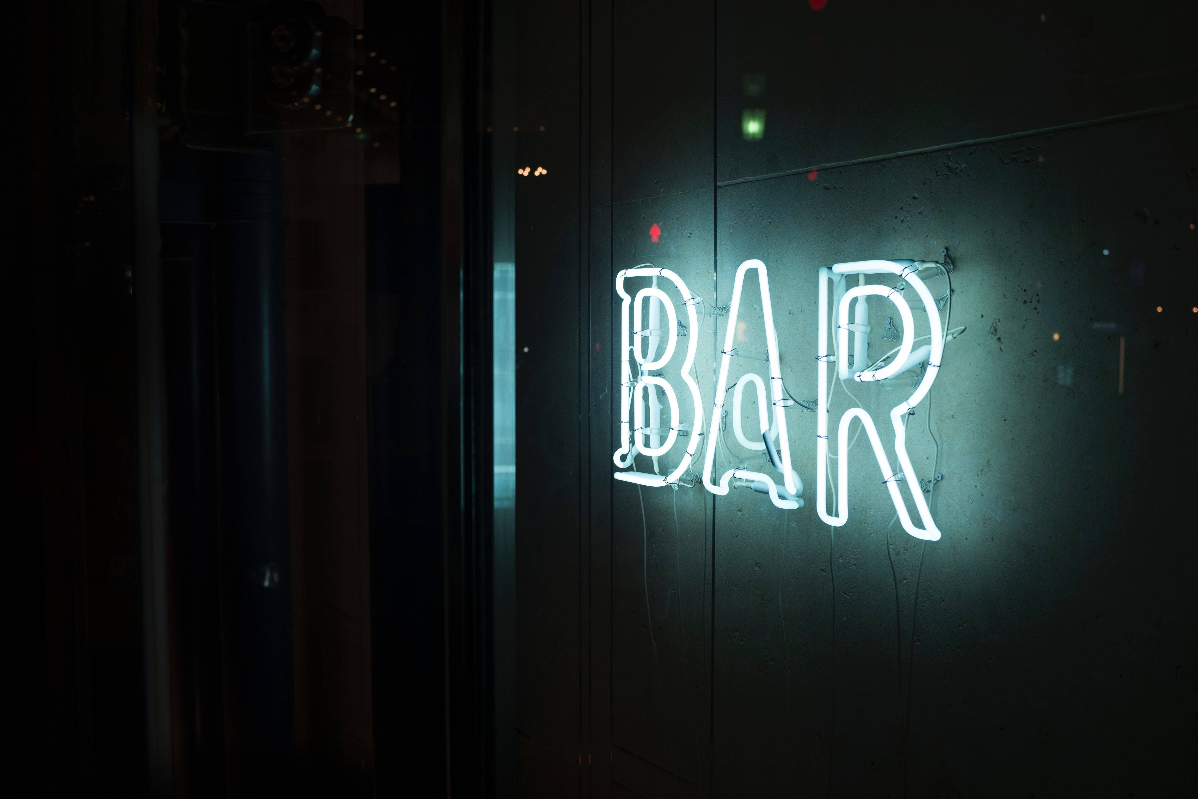 酒吧霓虹燈 壁紙 — 一個發光的白色霓虹燈牌，拼寫著BAR，在夜晚將冷光投射在深色紋理牆上。