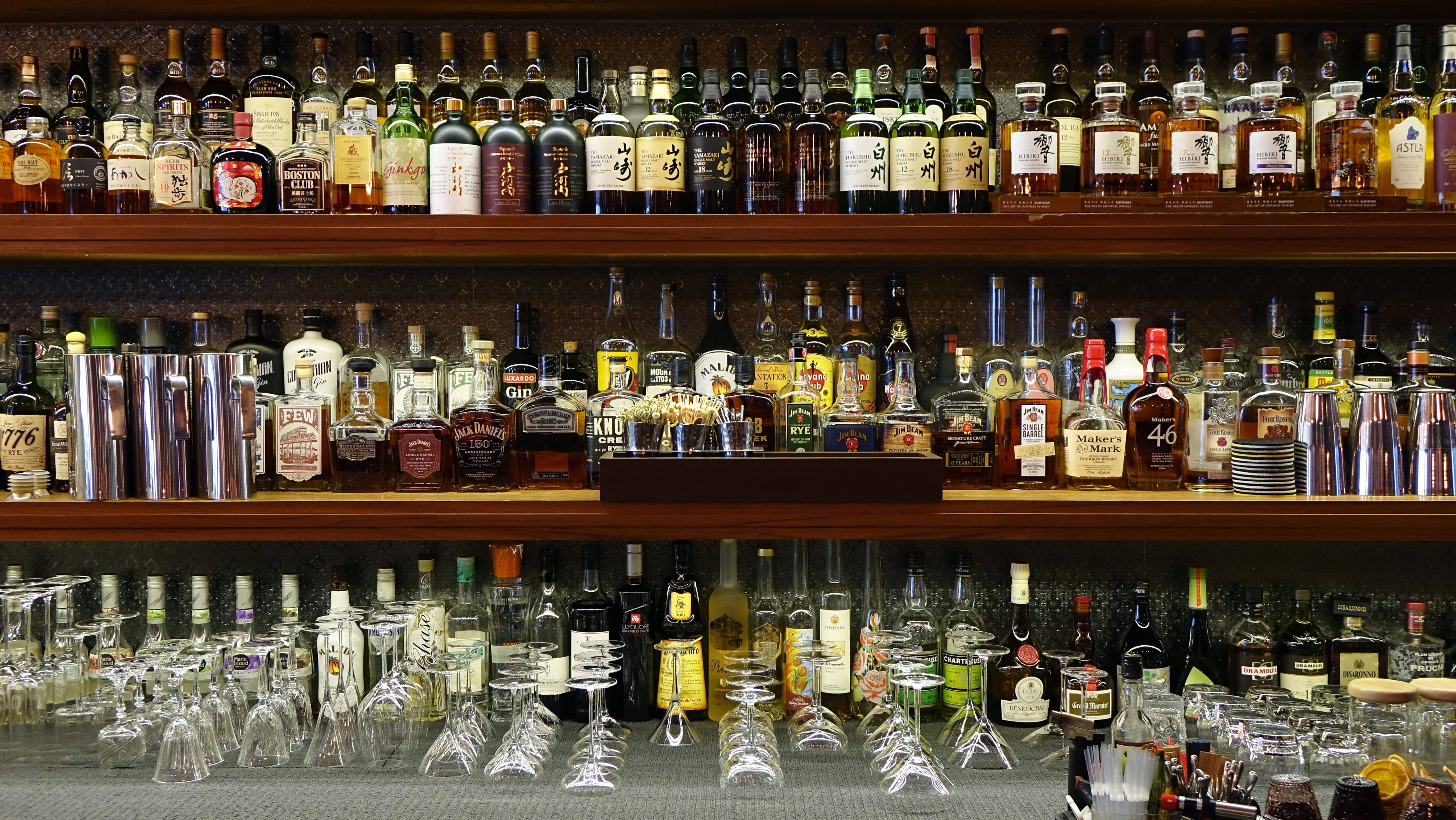 酒吧飲品與配件 壁紙 — 一排排酒瓶和雞尾酒杯整齊地排列在吧檯後方的木架上。