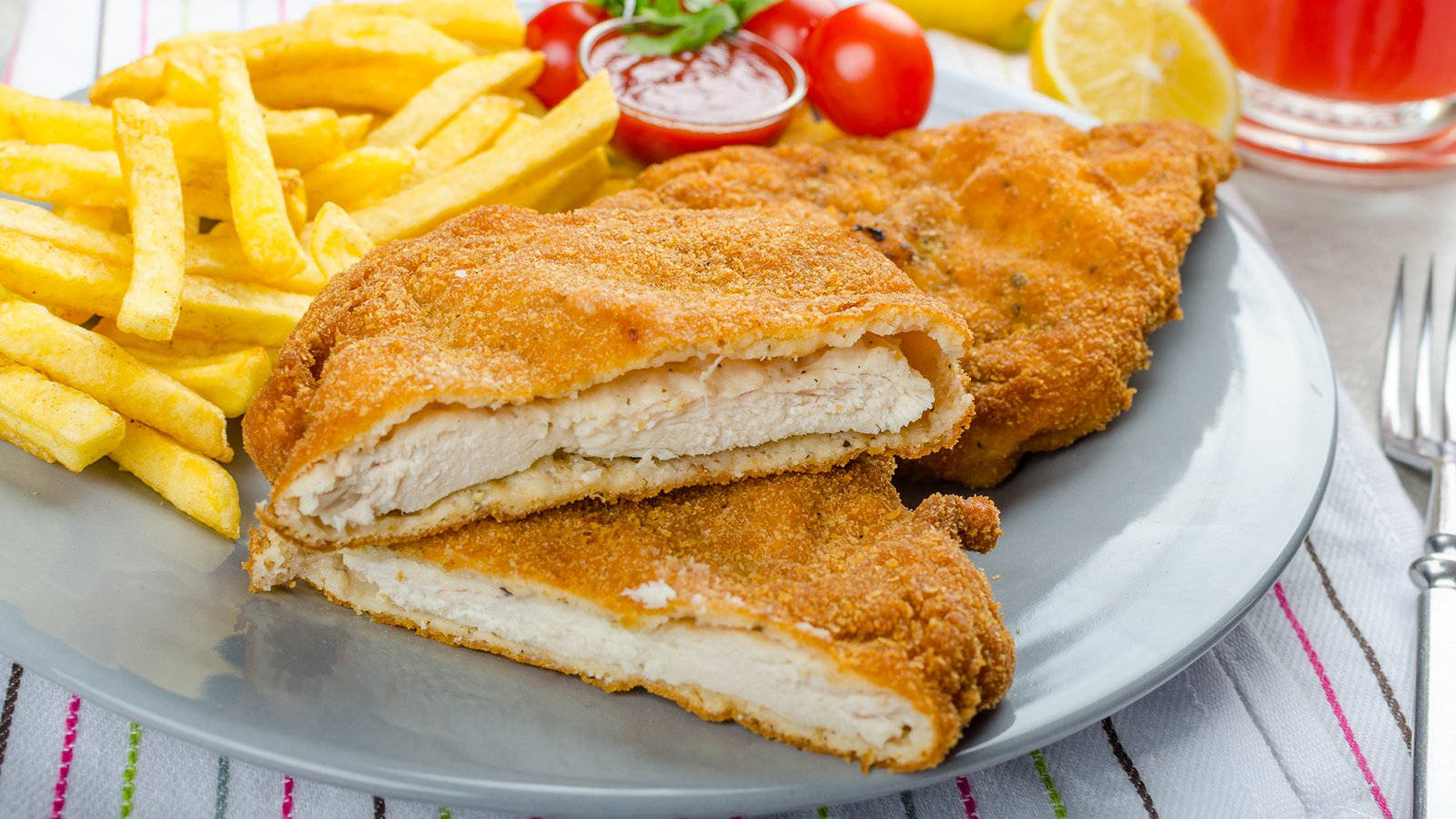 酥炸維也納炸肉排 壁紙 — 金黃色的炸雞扒切開，露出嫩滑的白肉，配上香脆薯條、車厘茄和茄汁，放在灰色碟上。