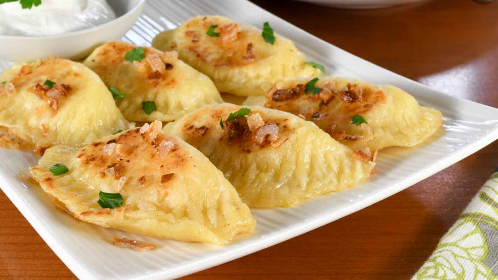 酥脆香煎餃子 壁紙 — 金黃色的波蘭餃子配上香脆洋蔥和新鮮歐芹，放在白色碟子上，令人垂涎。