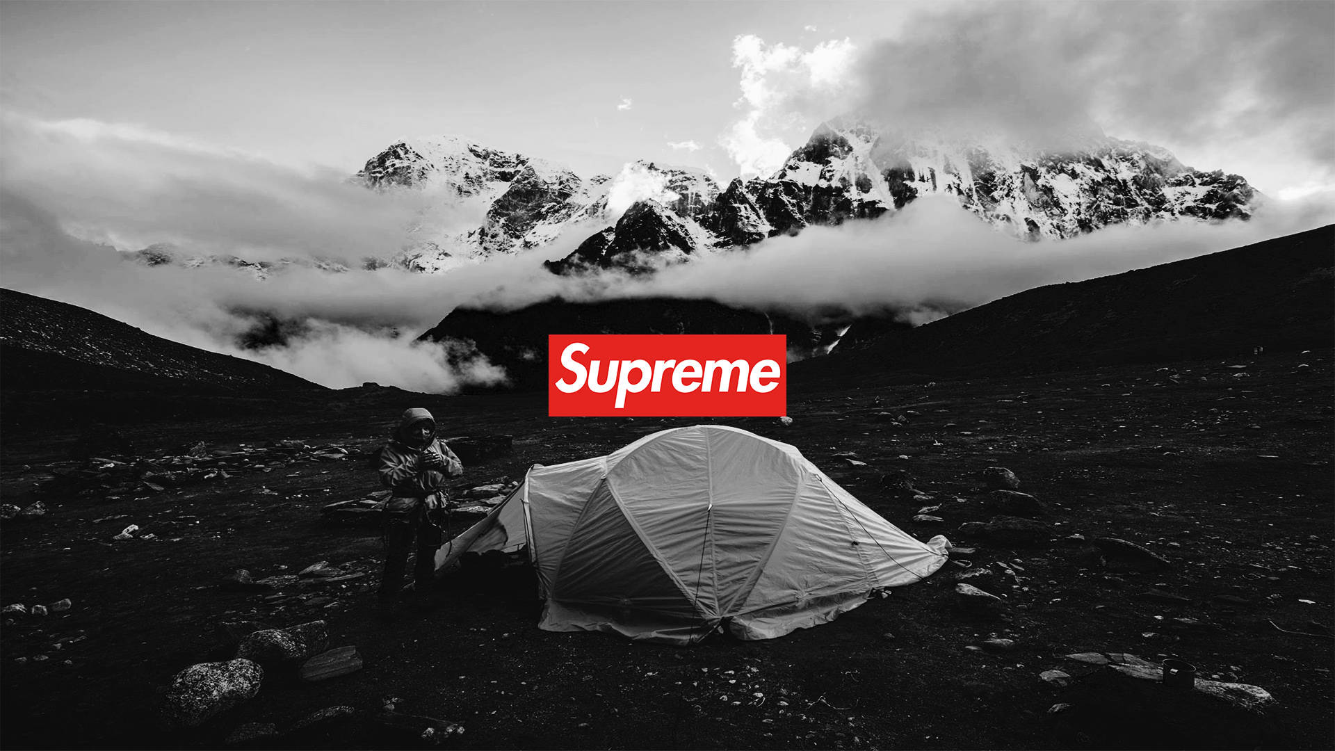 酷 Supreme 帳篷 壁紙 — 一個孤獨的遠足者站在帳篷旁邊，在一個黑白分明的山谷中，有積雪的山峰和雲朵，下方是一個大膽的紅色Supreme標誌。