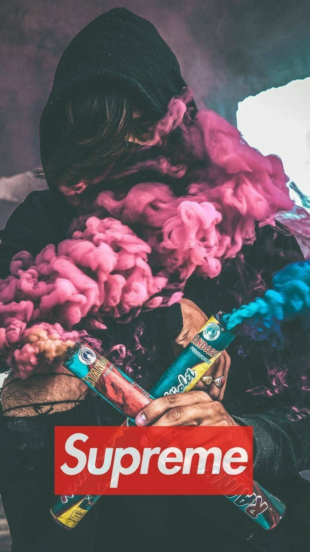 酷 Supreme 彩色煙霧幕 壁紙 — 一個戴著兜帽的人物呼出鮮豔的粉紅色和藍色煙霧，同時手持兩個帶有紅色 Supreme 標誌疊加的煙霧彈。