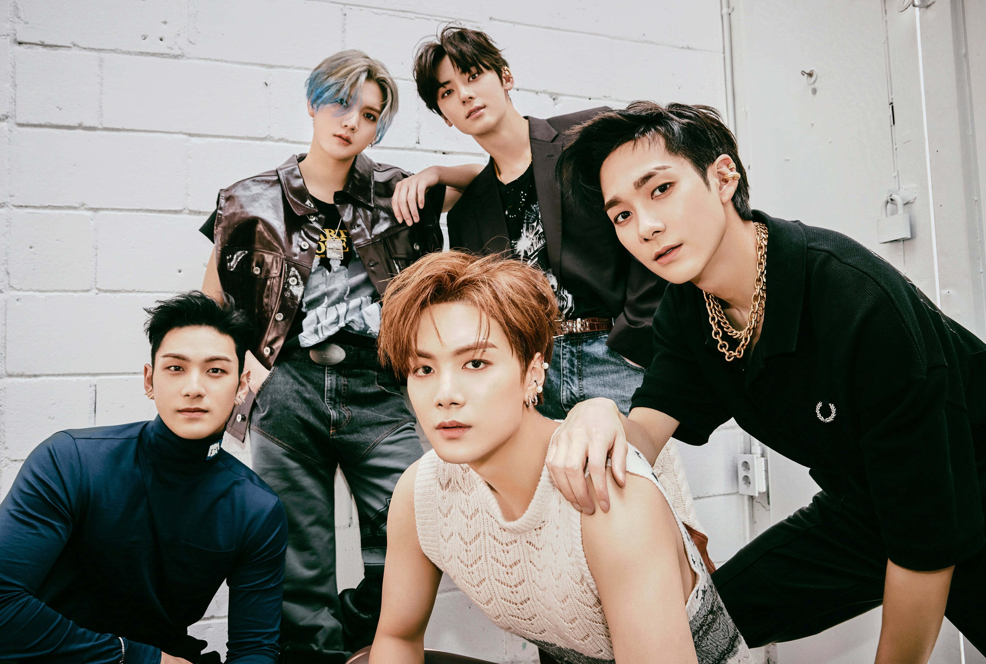 酷感 NUEST KPOP 男子團體 壁紙 — 五位時尚年輕男子，擁有繽紛髮色和前衛造型，自信地在白色磚牆前擺姿勢。