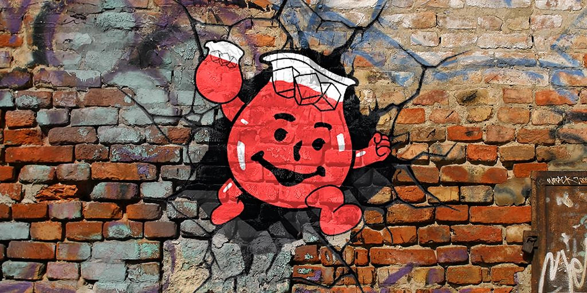酷樂飲料人塗鴉 壁紙 — 一個開心的紅色卡通角色在充滿活力的塗鴉藝術中衝破裂開的磚牆。