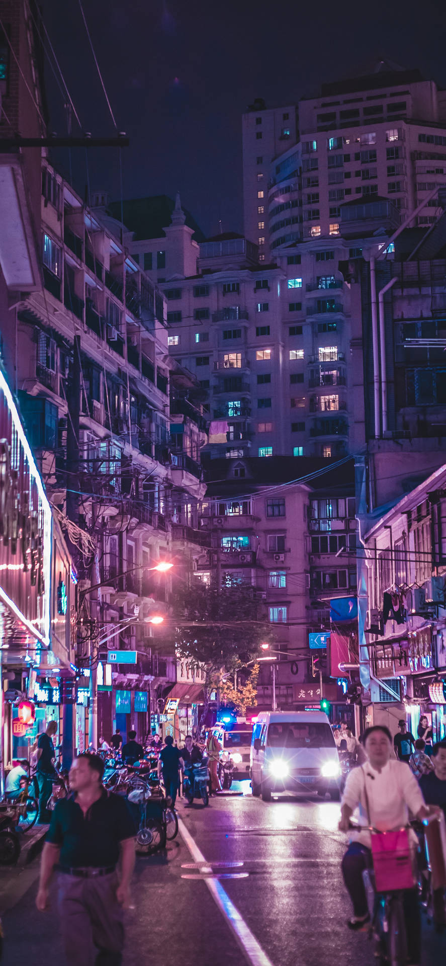夜晚嘅城市街道，有發光嘅霓虹招牌同行路同踩單車嘅人。