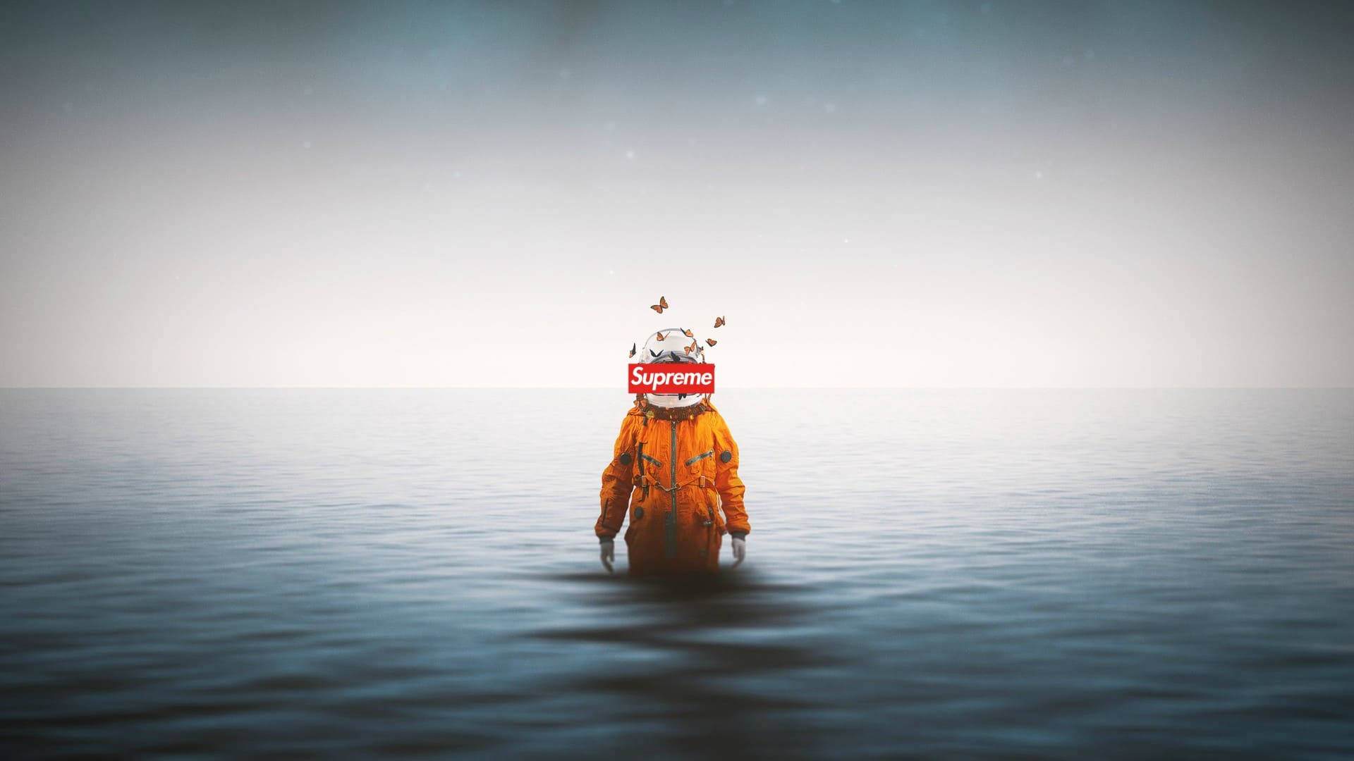 酷炫 Supreme 太空人海洋 壁紙 — 一個穿著橙色太空衣的人站在平靜的海水中，水深及腰，頭戴Supreme標誌頭盔，蝴蝶從頭盔中飛出。